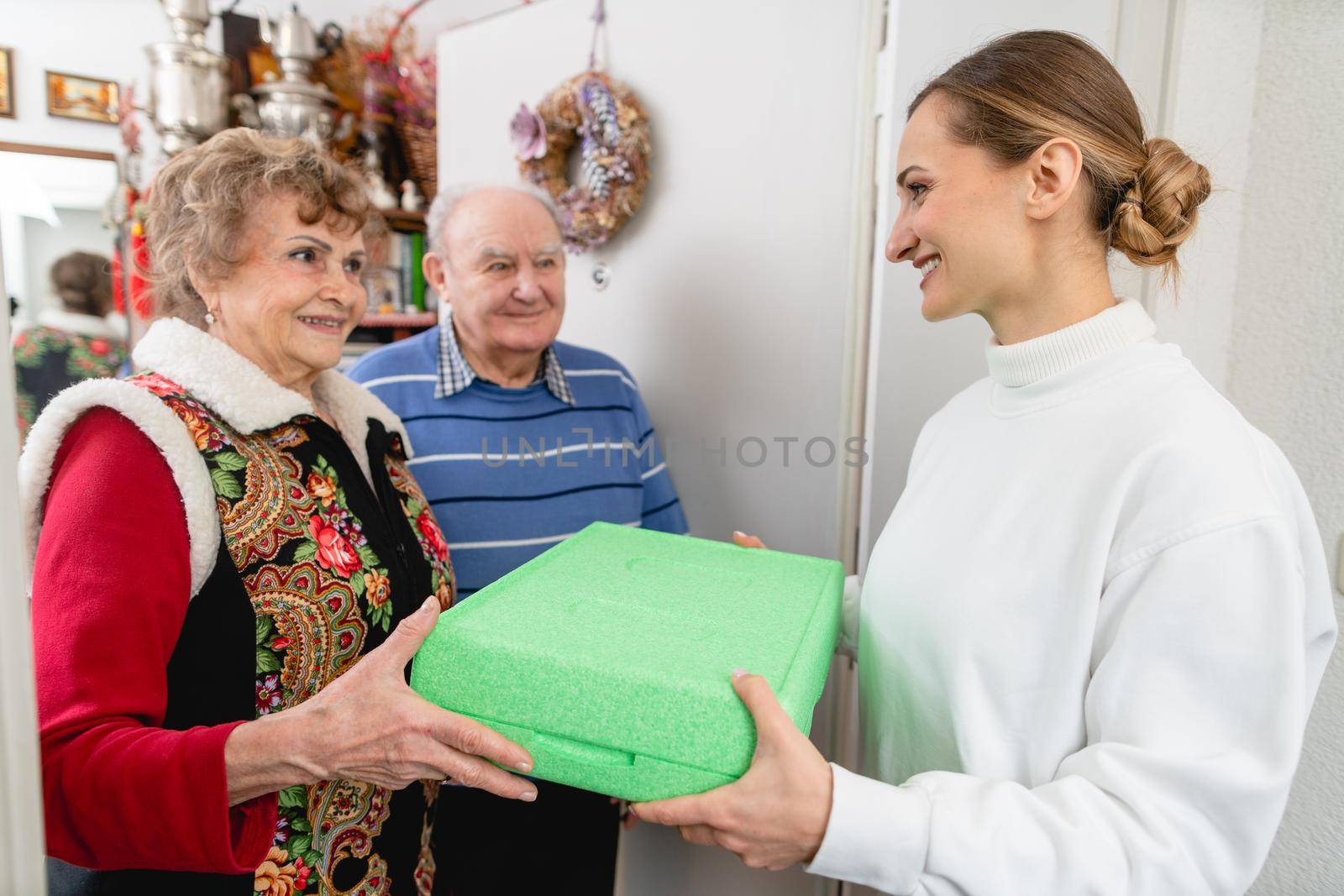 Senior couple greeting volunteer woman delivering a hot meal to their door