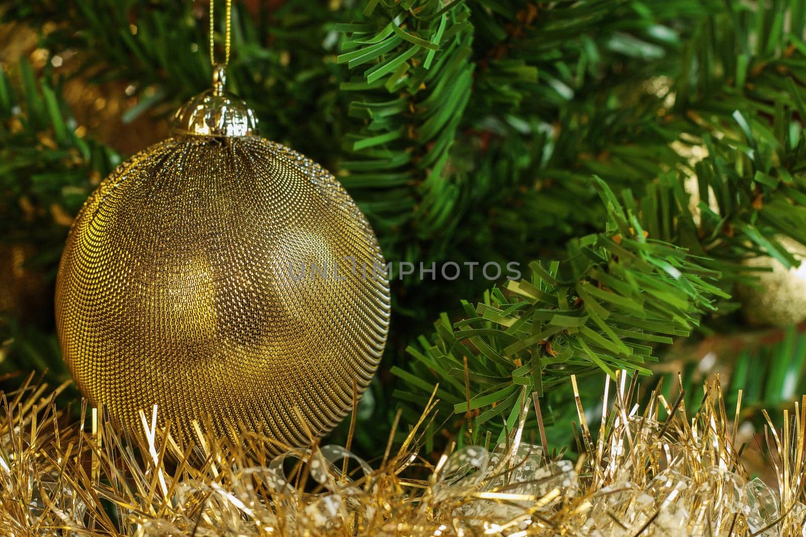 Horizontal image of the detail of golden decoration on the christmas tree with gold chain. Gold and green colours 