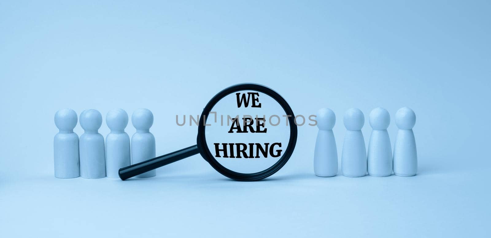 wooden figures of men stand on a blue background and a black magnifying glass. Recruitment concept, search for talented and capable employees, career growth