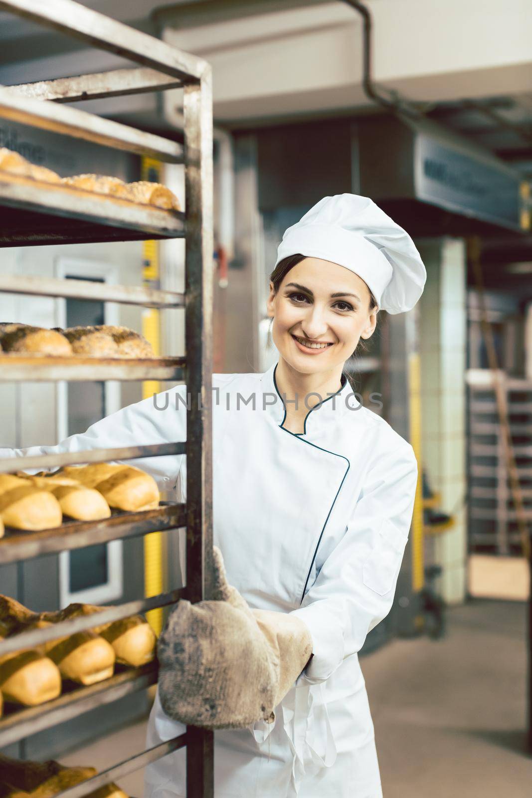 Baker woman pushing sheets with bread in the baking oven by Kzenon