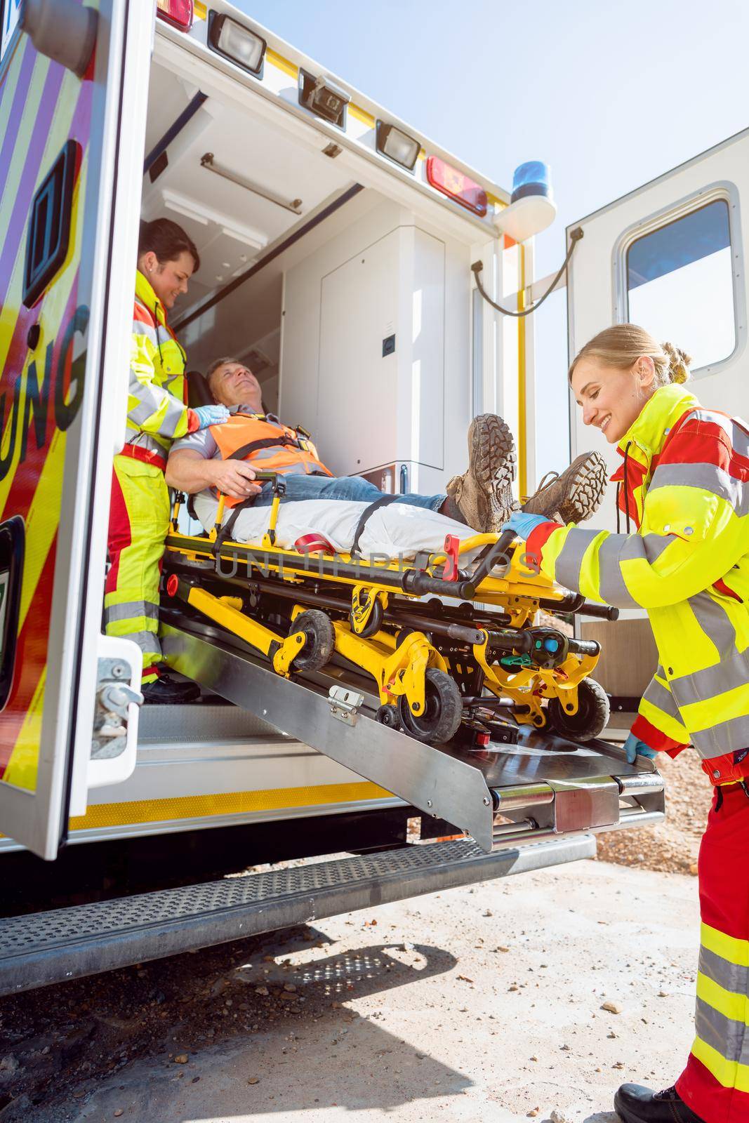 Paramedics putting injured man on stretcher in ambulance car by Kzenon