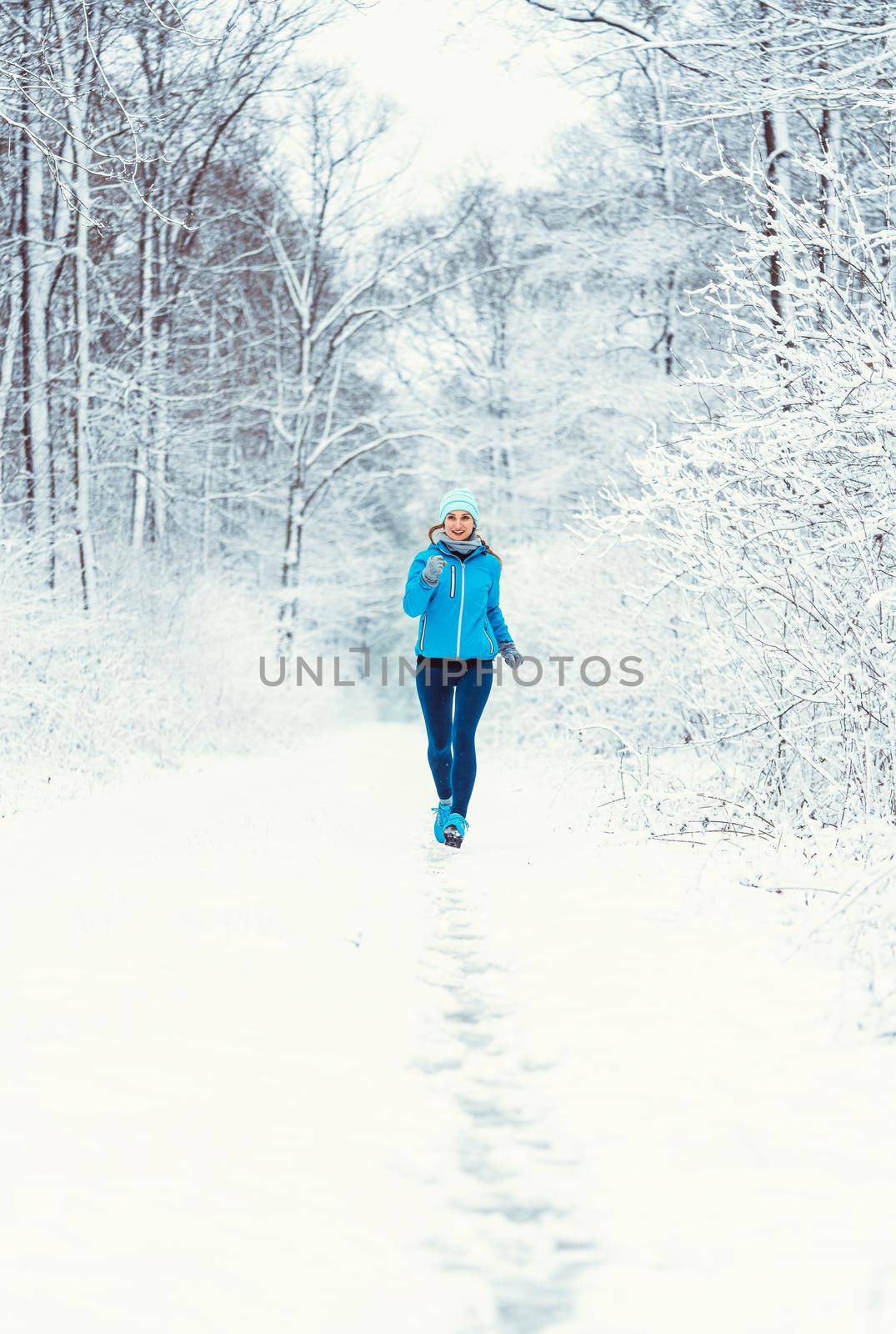 Woman jogging towards camera in cold and snowy forest for fitness gains