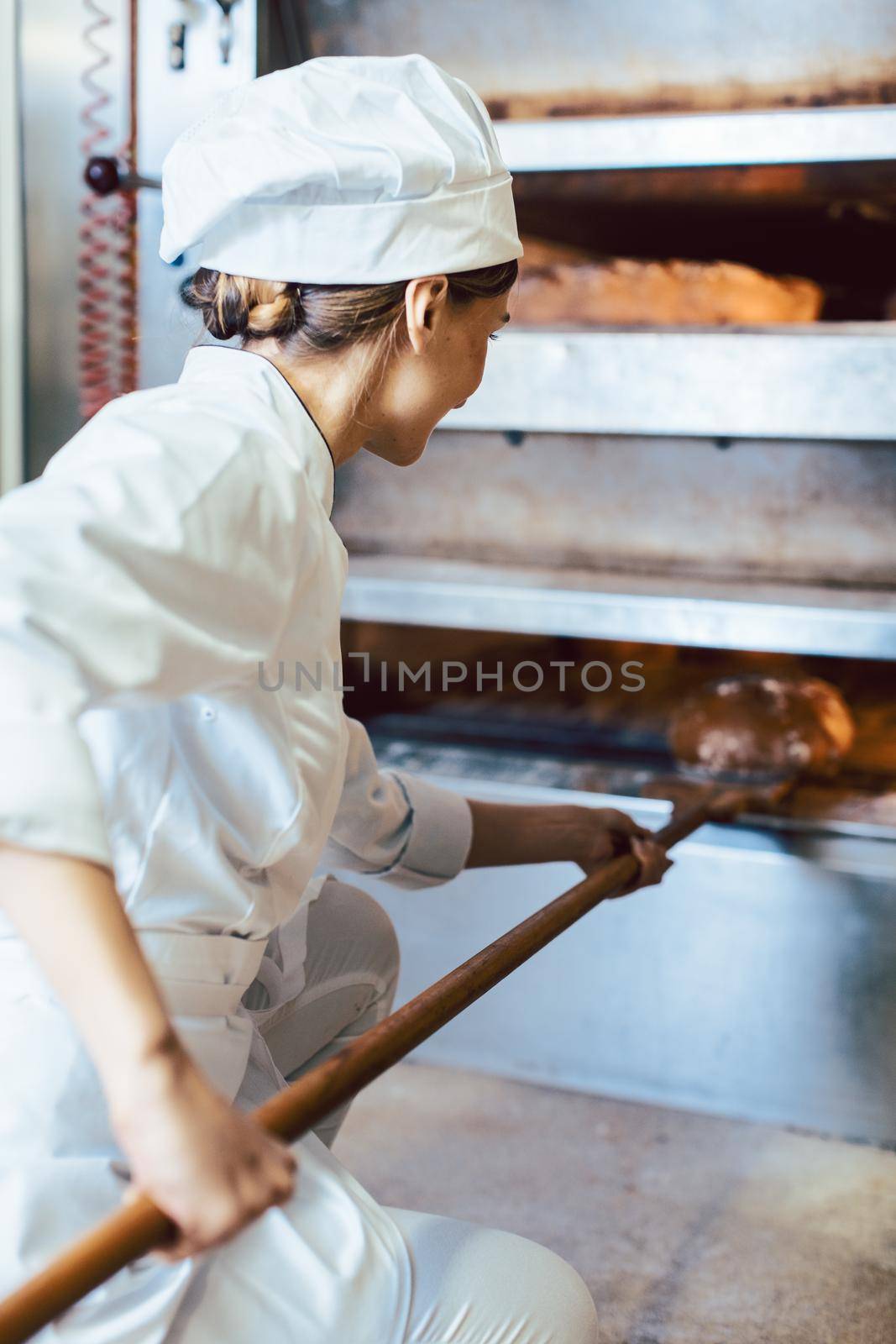 Baker putting bread in the bakery oven by Kzenon