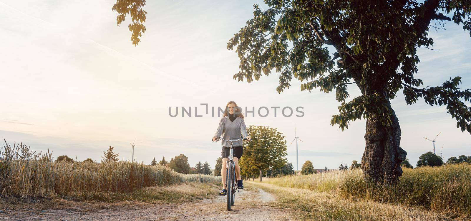 Woman on a bicycle having fun in rural landscape during sunset