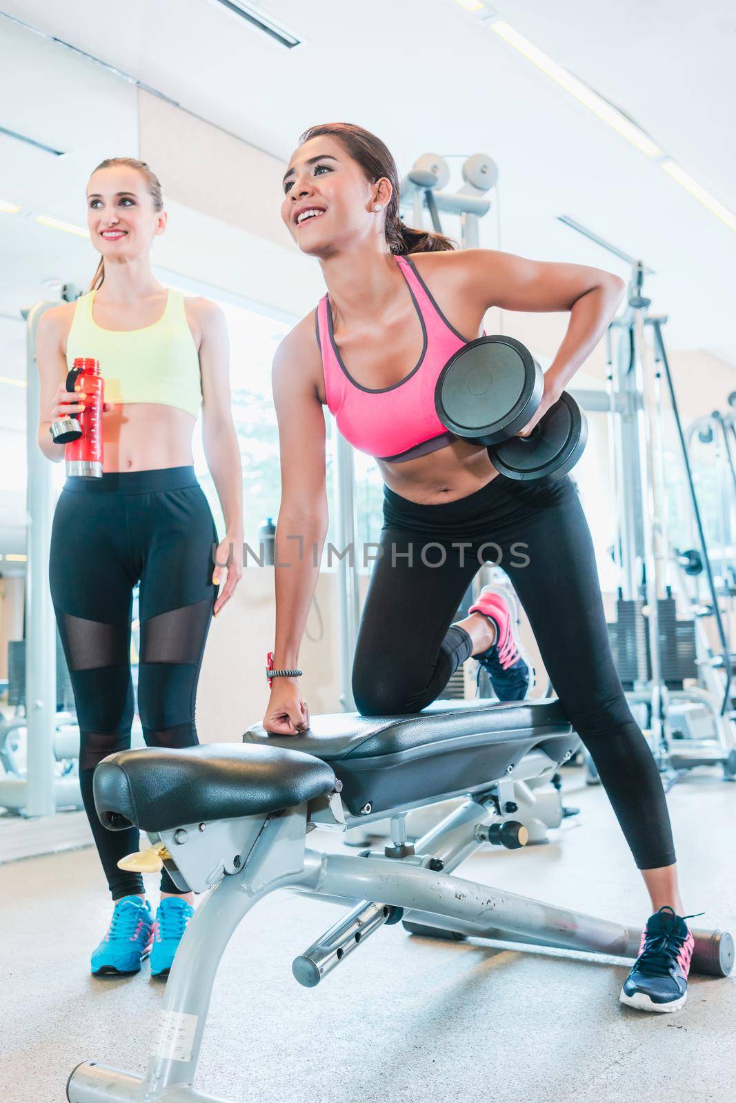 Powerful young woman smiling while rowing with one arm in a trendy health club by Kzenon