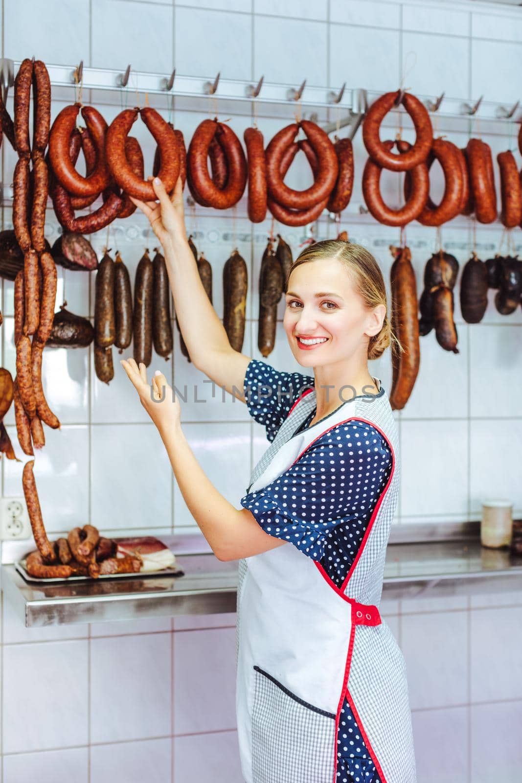 Woman actively recommending sausages in her butchery shop taking them from the hook