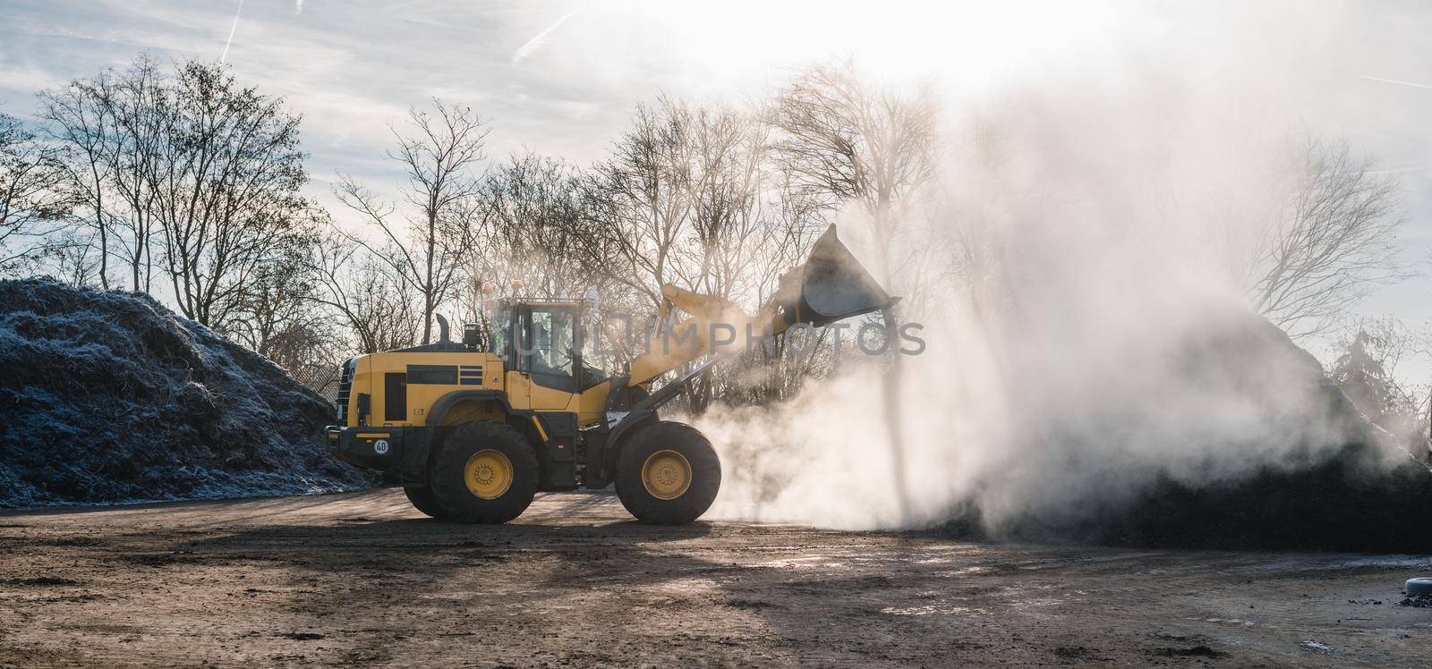 Wheel loader working on heap with biomass for composting on bright sunny day