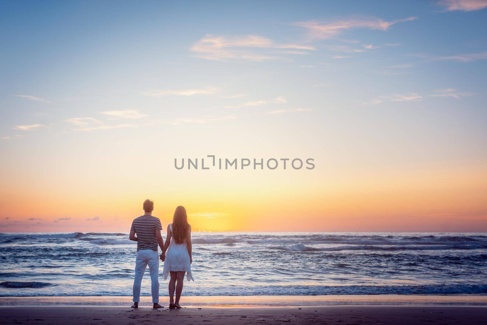 Romantic couple holding hands in their vacation standing on a beach by the sea