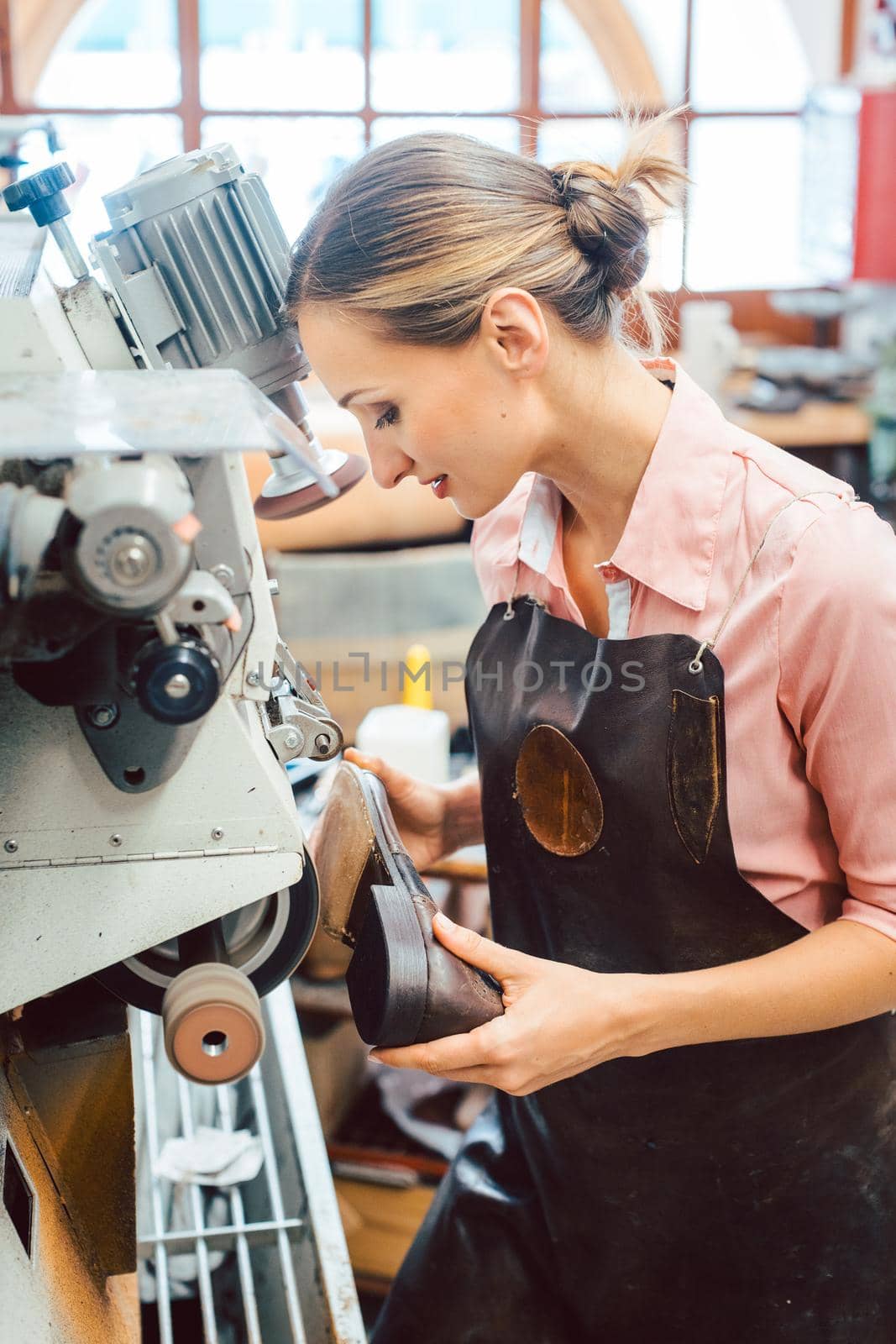 Woman cobbler working on machine in her shoemaker workshop adjusting the settings