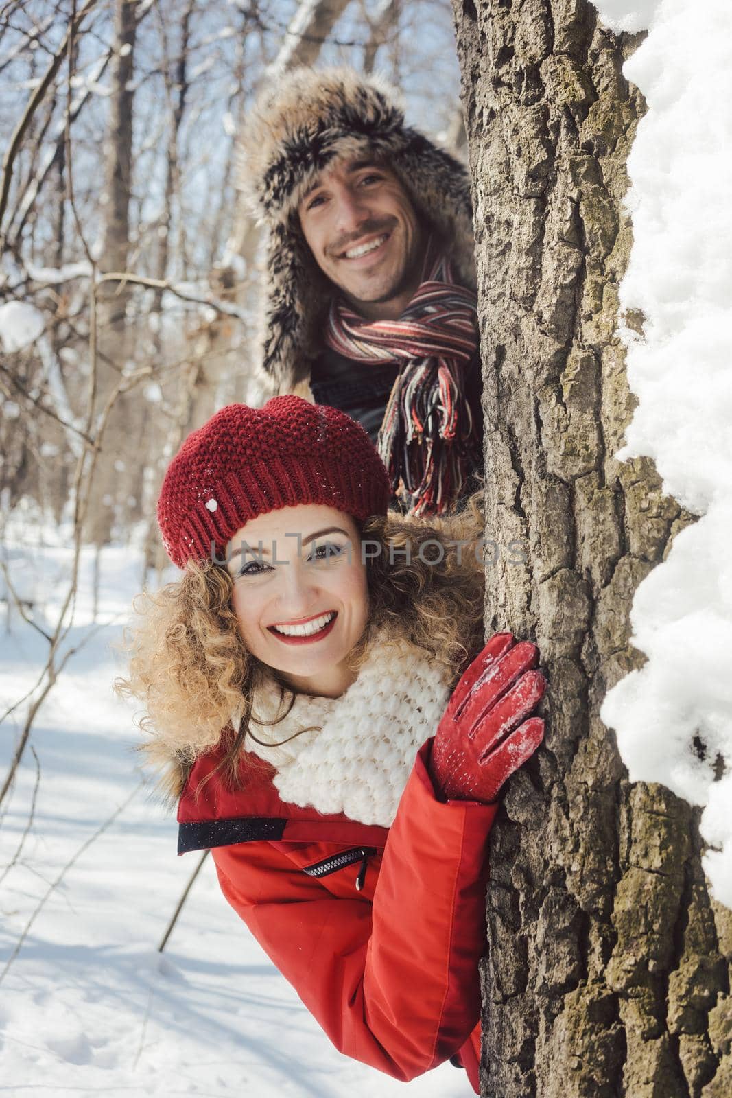 Playful couple in the snow hiding behind a tree trunk by Kzenon