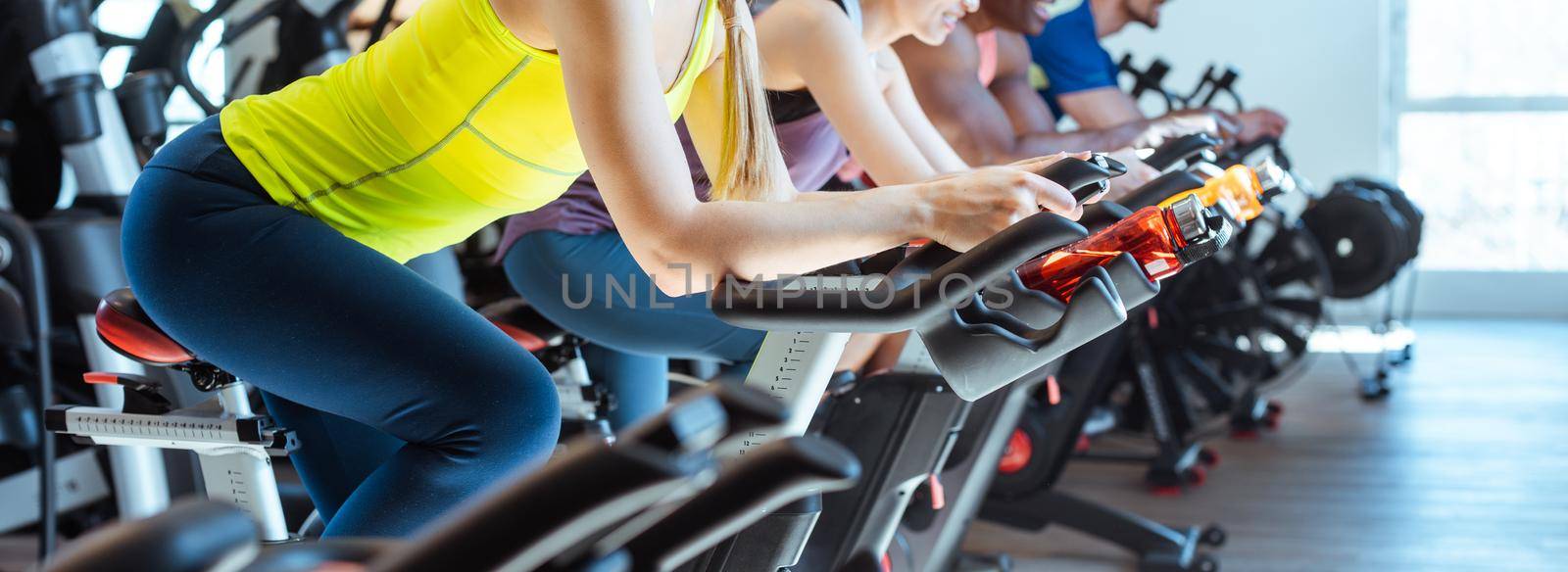 Very fit Caucasian woman and her friends on fitness bike in gym