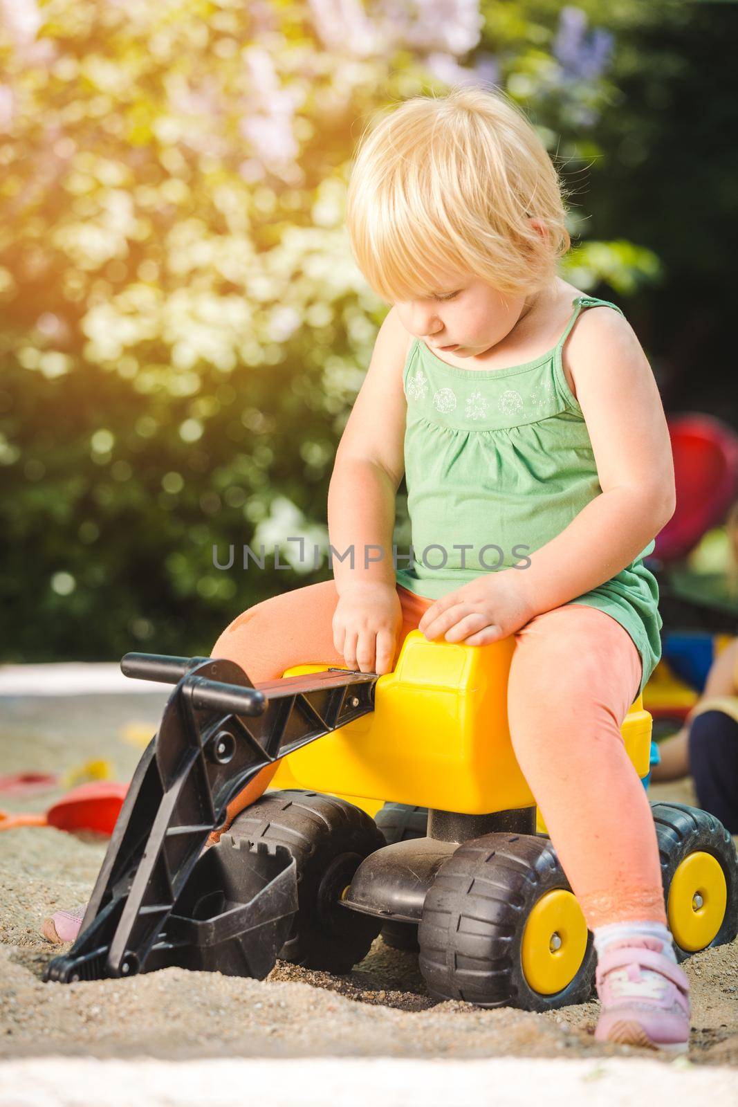 Girl child riding on a yellow toy tractor on playground