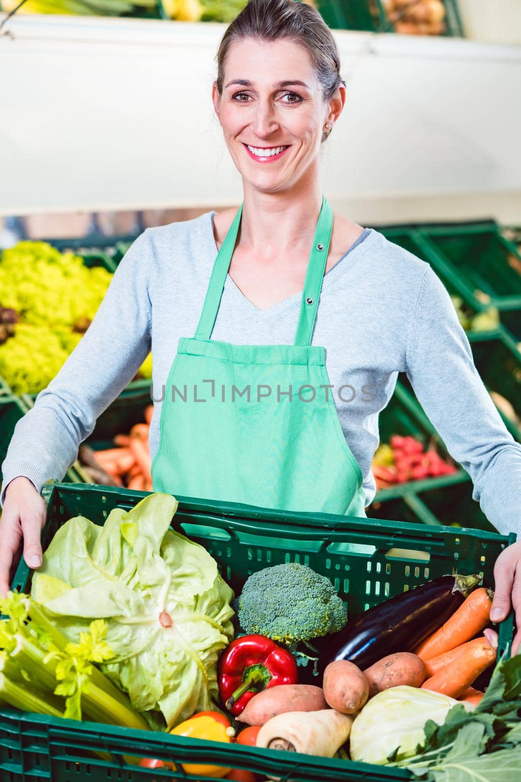 Cheerful saleslady holding box with organic vegetables in shop