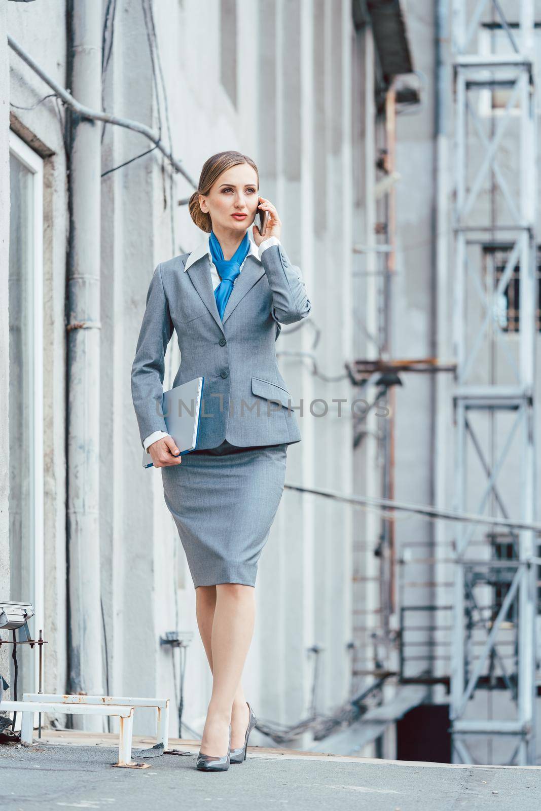 Business woman using her phone and holding a laptop in an industrial environment