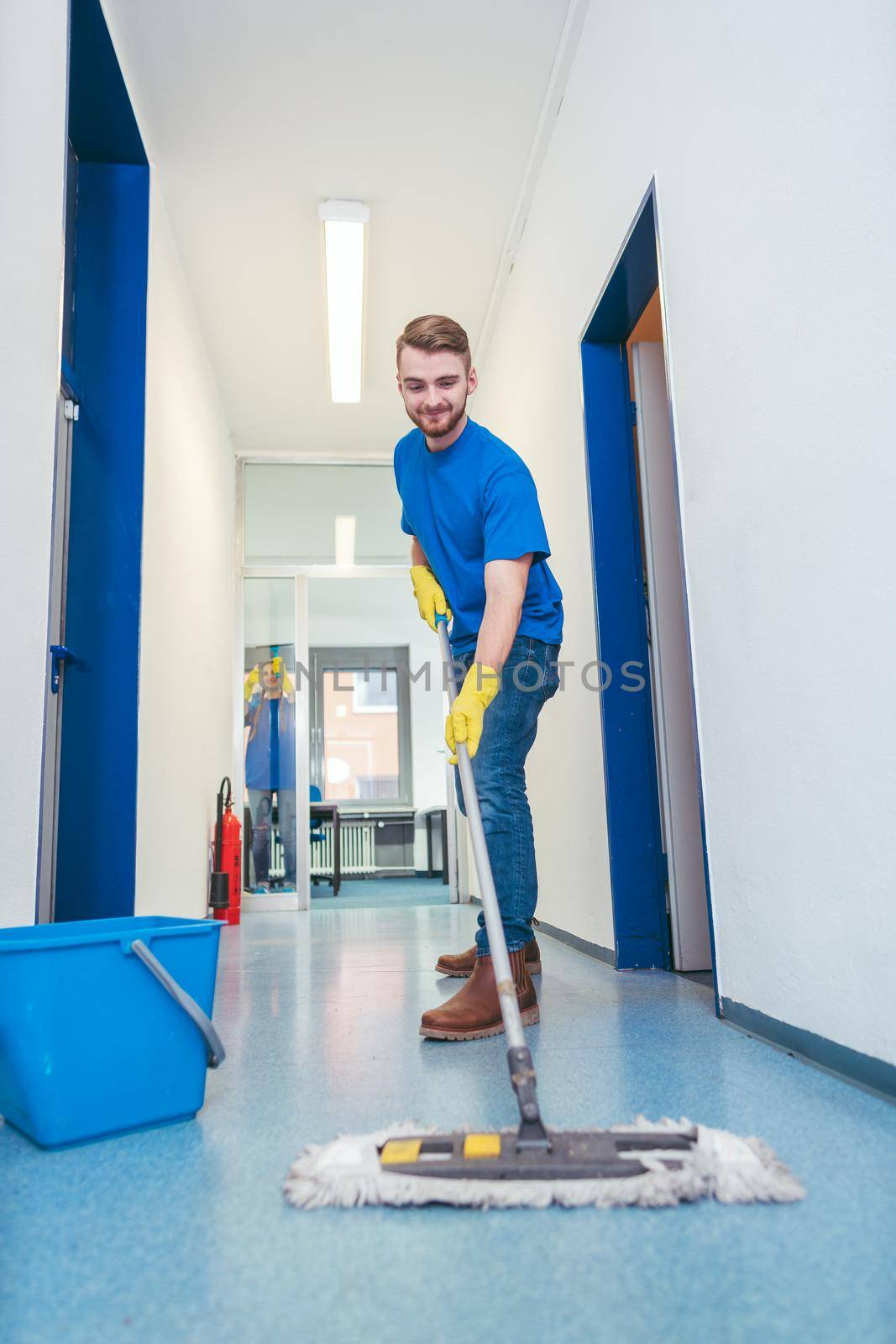 Cleaner man mopping the floor in a hall by Kzenon