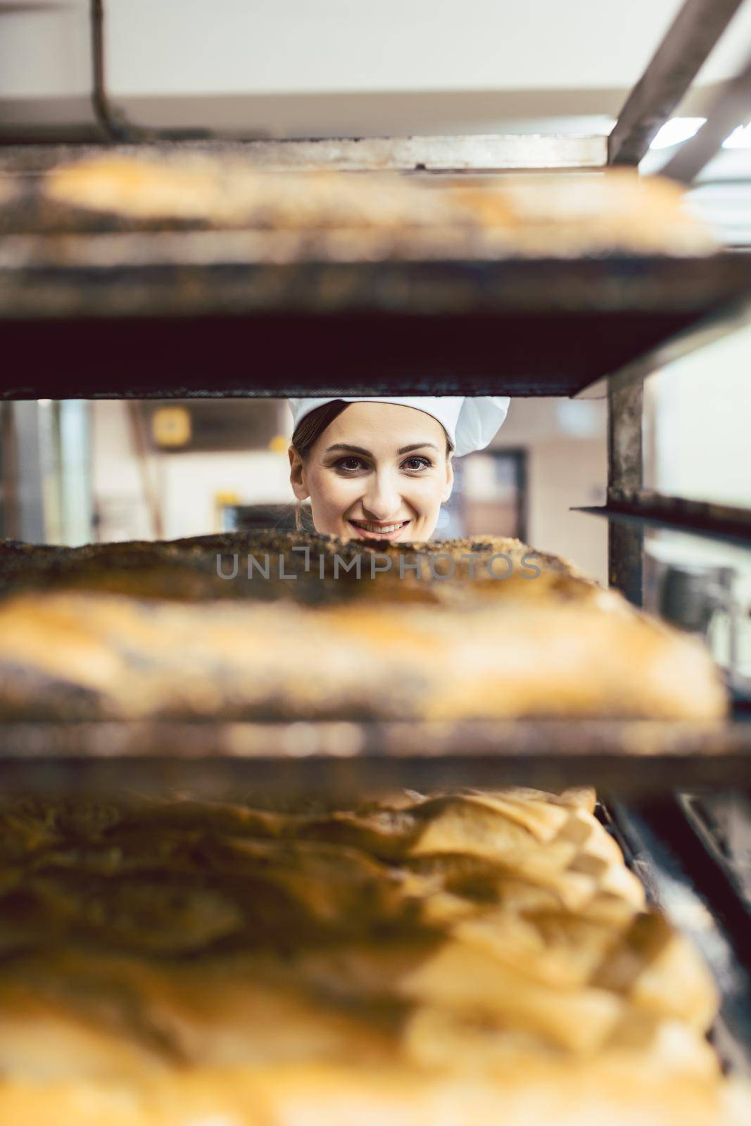 Beautiful baker woman looking though bread on sheets, focus on her face