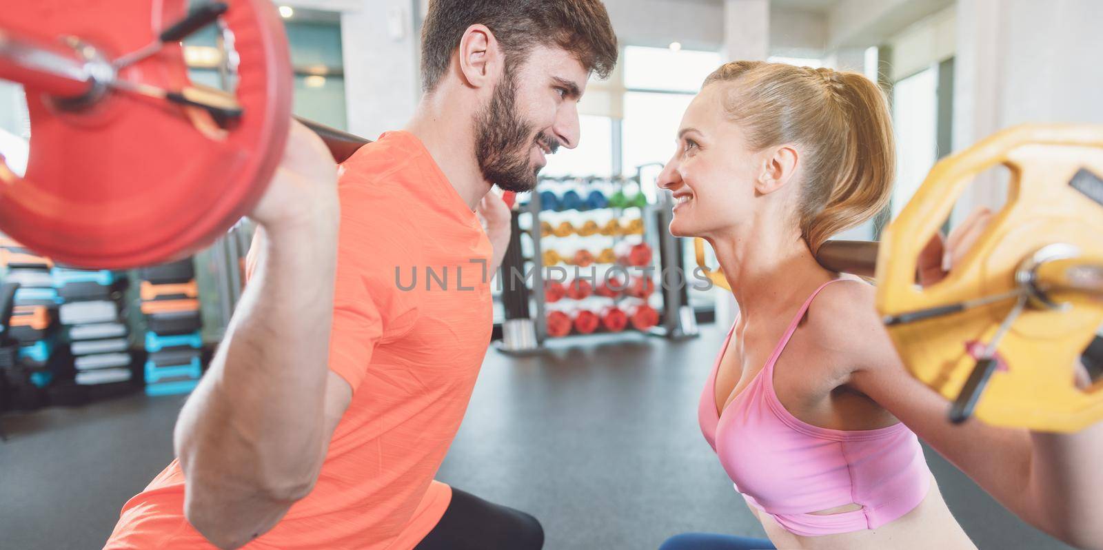 Couple of woman and man in the gym with weights in competition by Kzenon