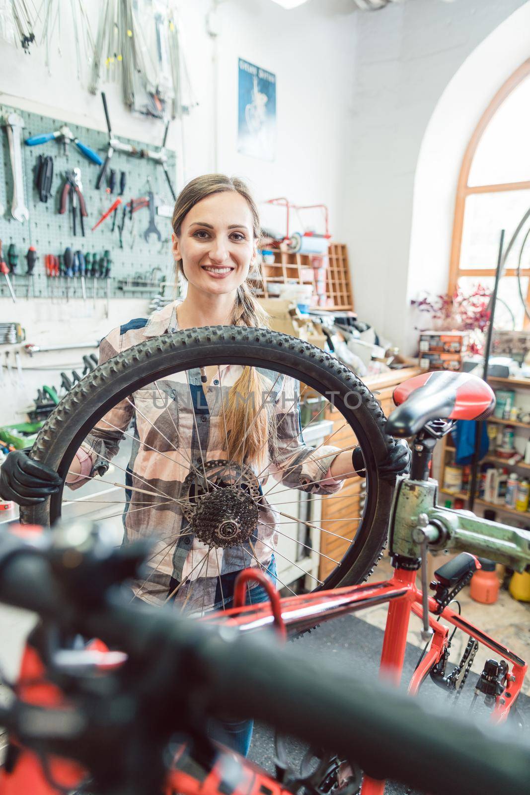 Bike mechanic woman looking through the wheel of bicycle by Kzenon