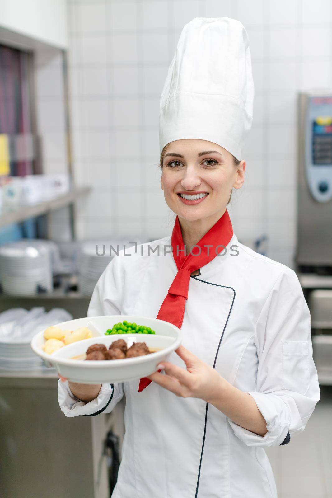 Proud cook showing plate with food in commercial kitchen of canteen
