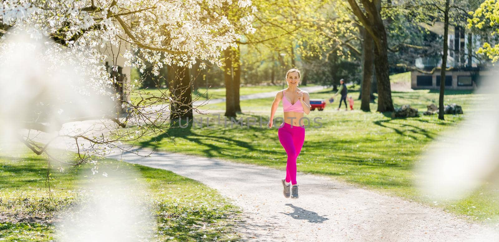 Fit woman running down a path towards camera during spring seen through blossom