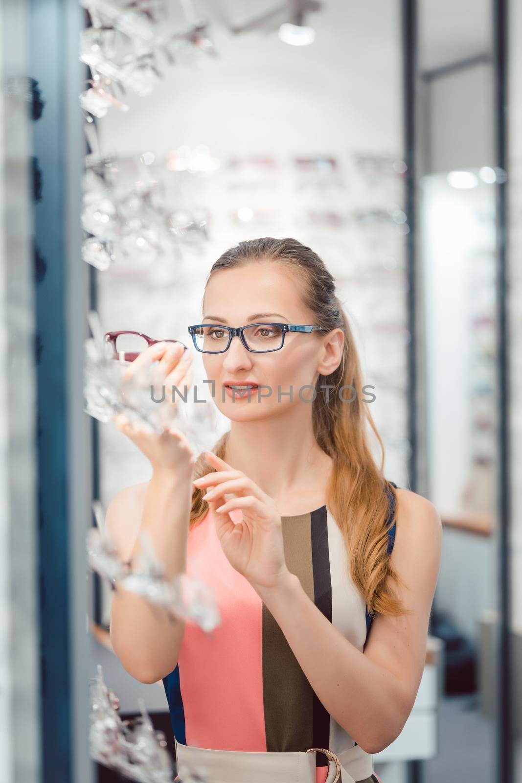 Woman being satisfied with the new eyeglasses she bought in the store holding them in front of her face