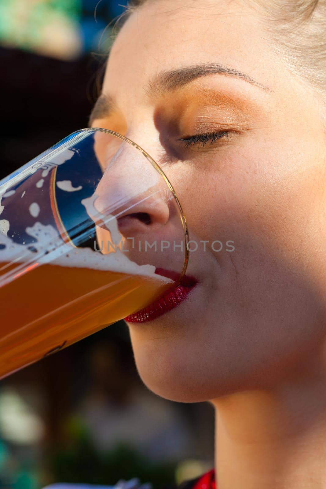 Side view closeup portrait of beautiful woman drinking beer on a sunny day with closed eyes