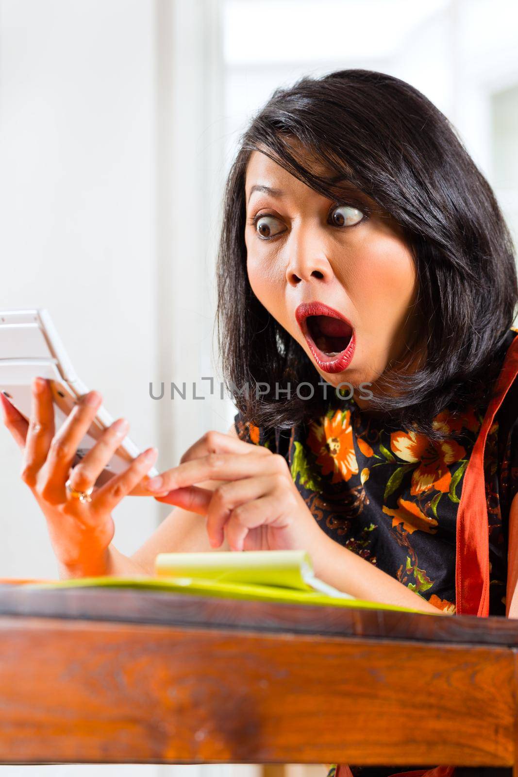 Close-up of shocked young woman looking at calculator holding in hand