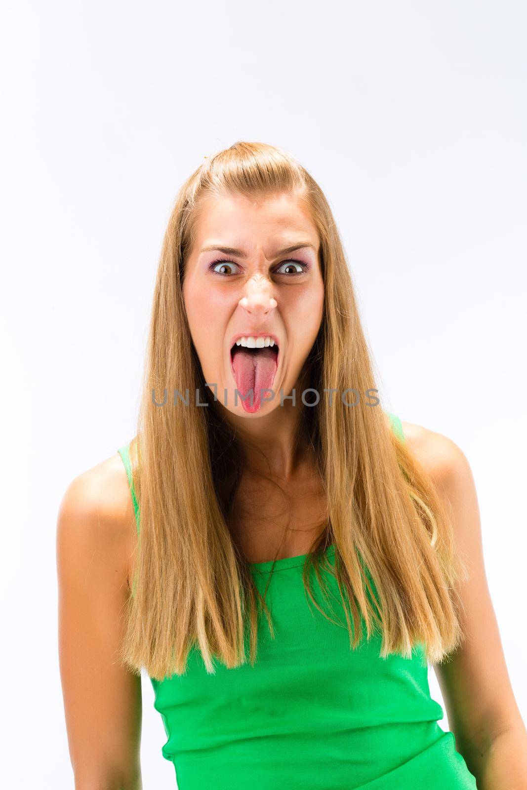 An angry young woman showing her tongue standing against white background