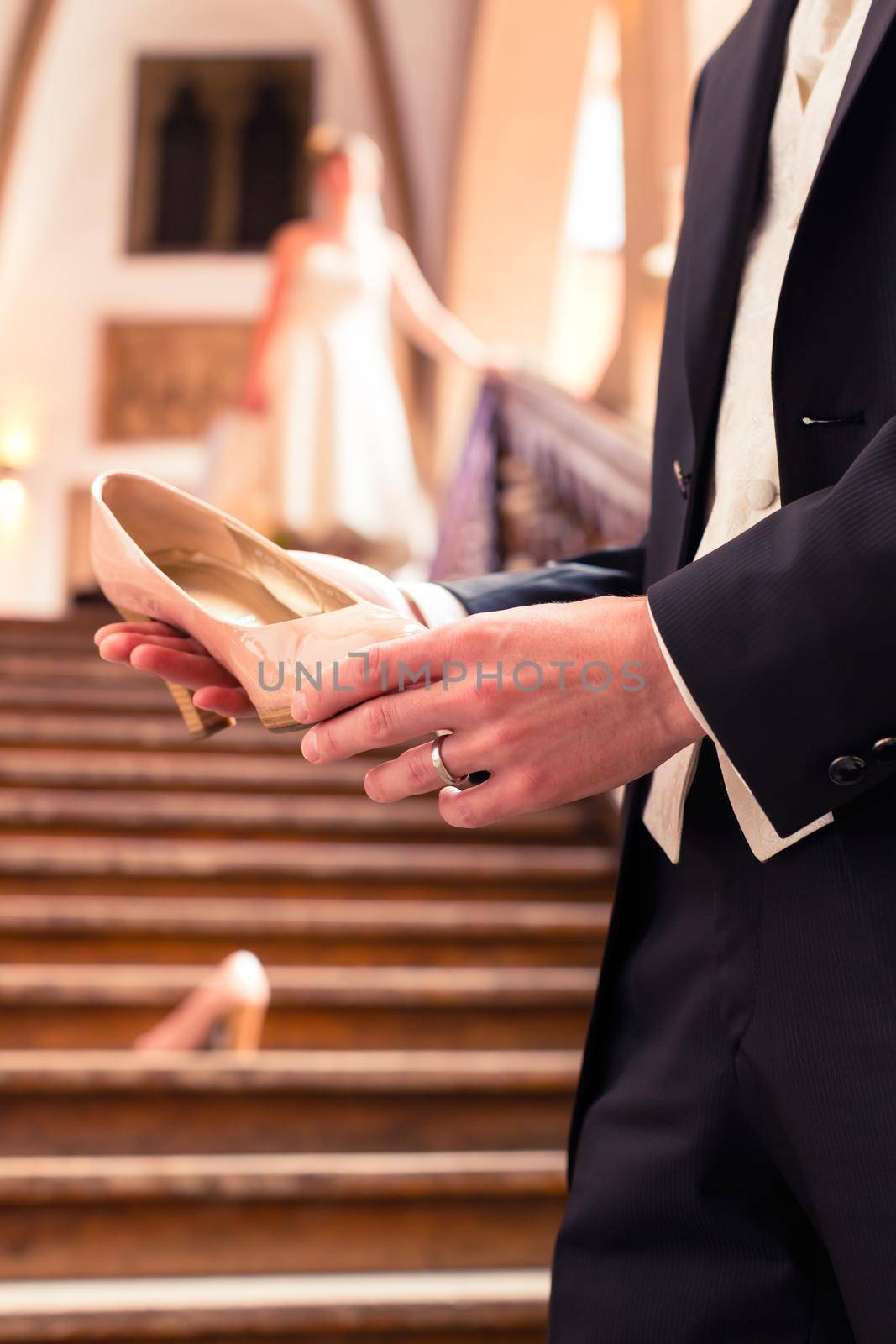 Close-up of bridegroom's hand holding bride's wedding shoe in front of staircase