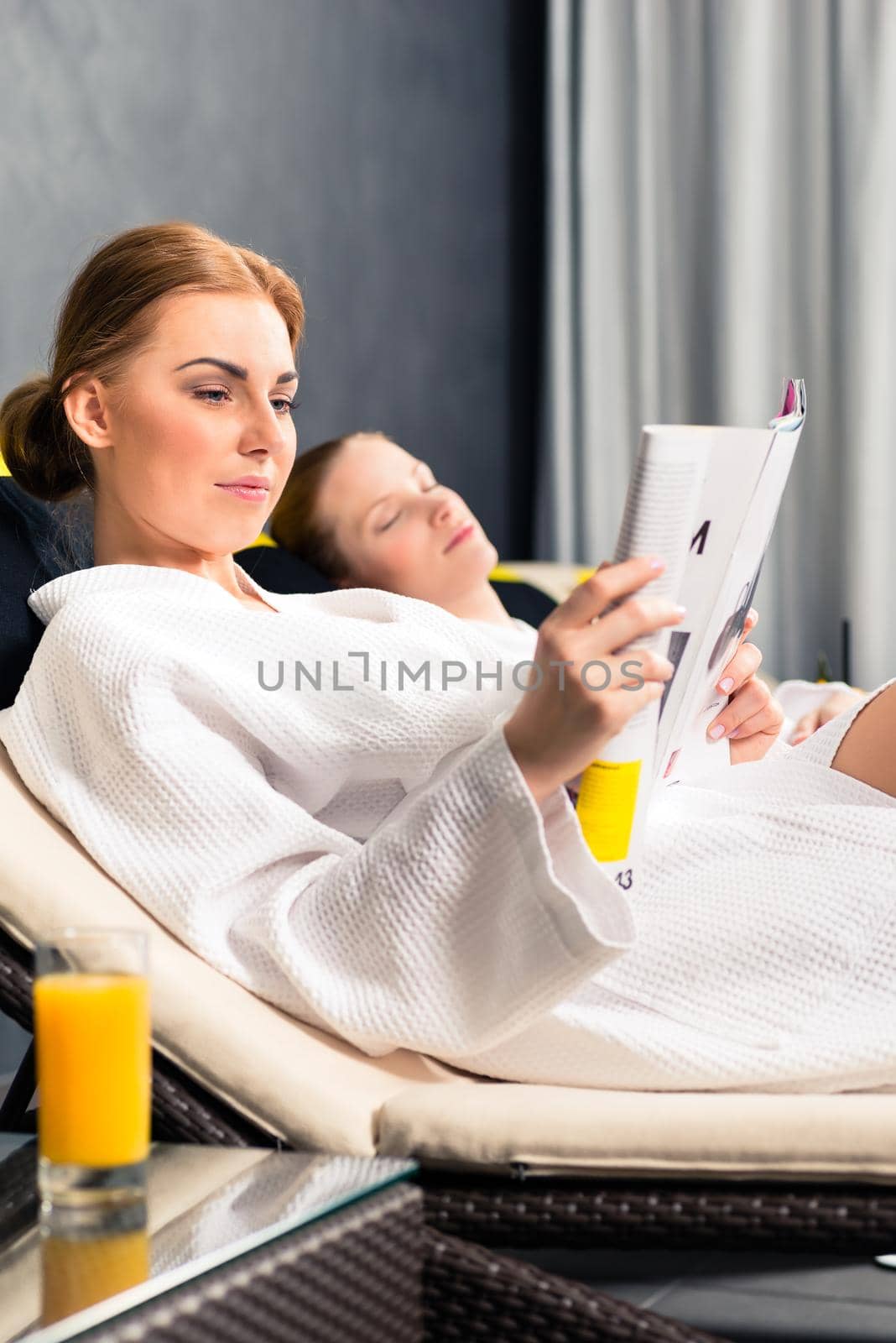 Woman in white bathrobe reading magazine book in spa