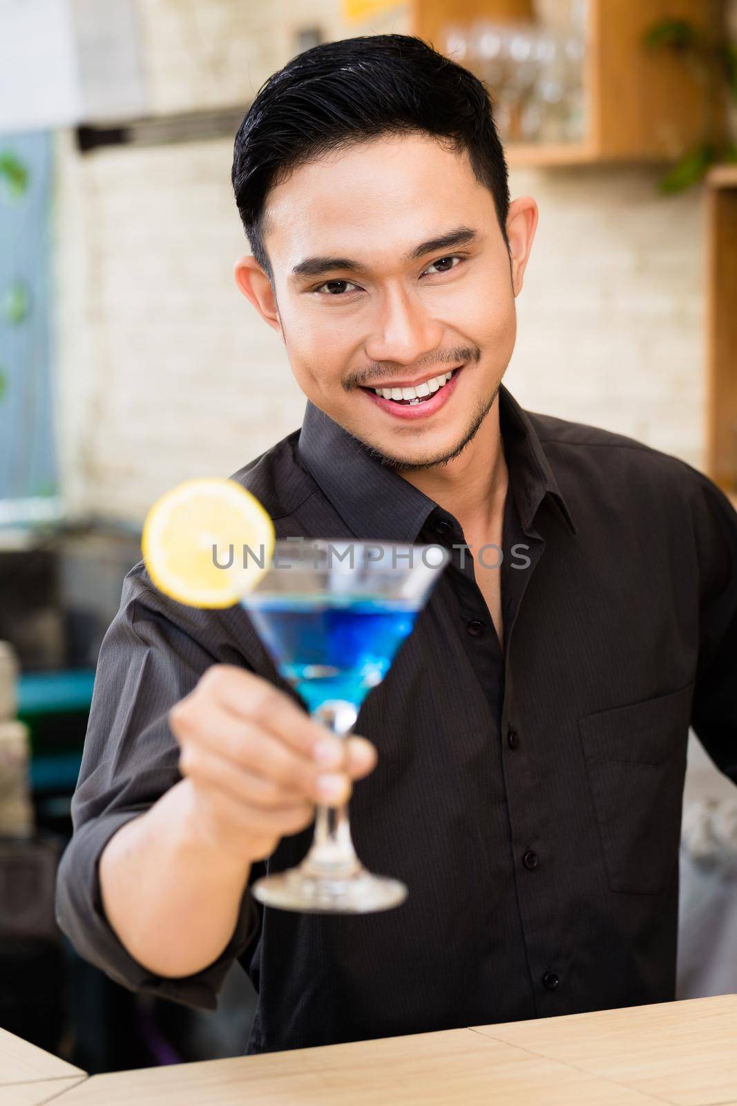 Portrait of handsome man holding blue cocktail at bar