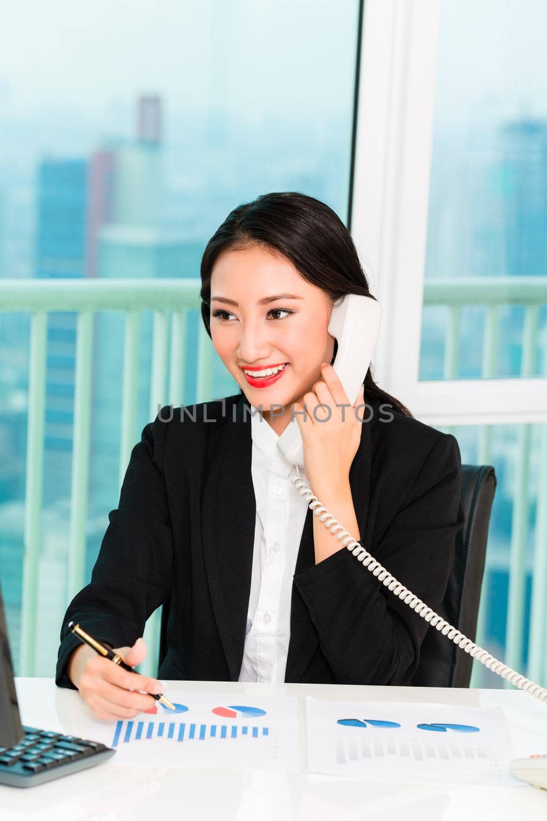 Young businesswoman talking on telephone with graph on desk in the office