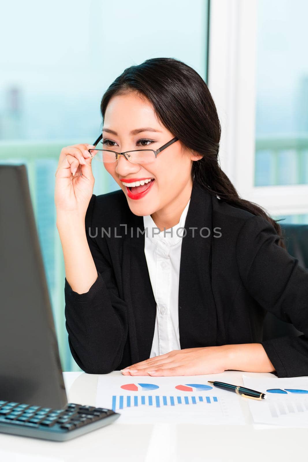 Young successful businesswoman looking at computer with pen, chart paper on the desk