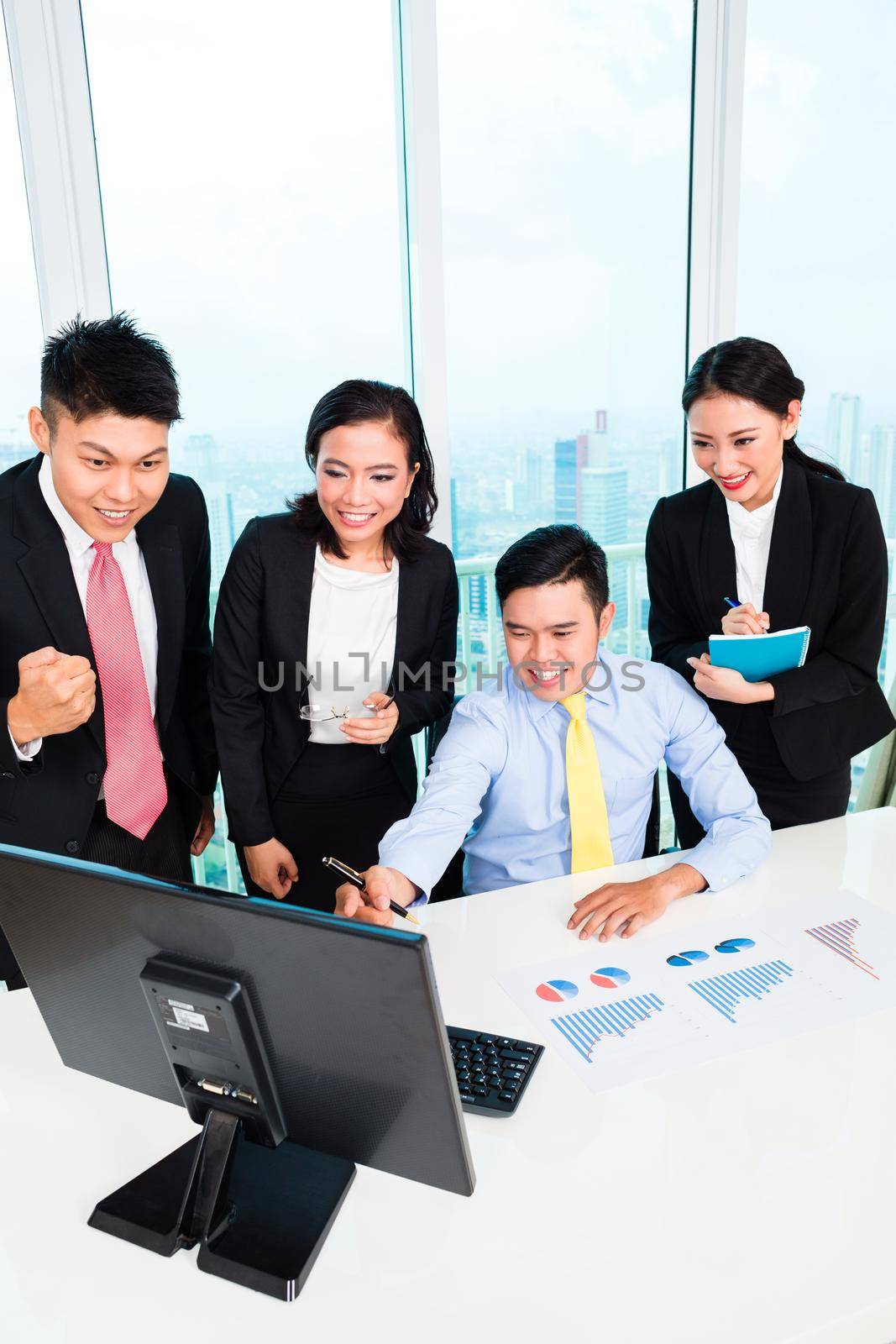 Group of businesspeople looking at computer with graph chart on the desk in the office