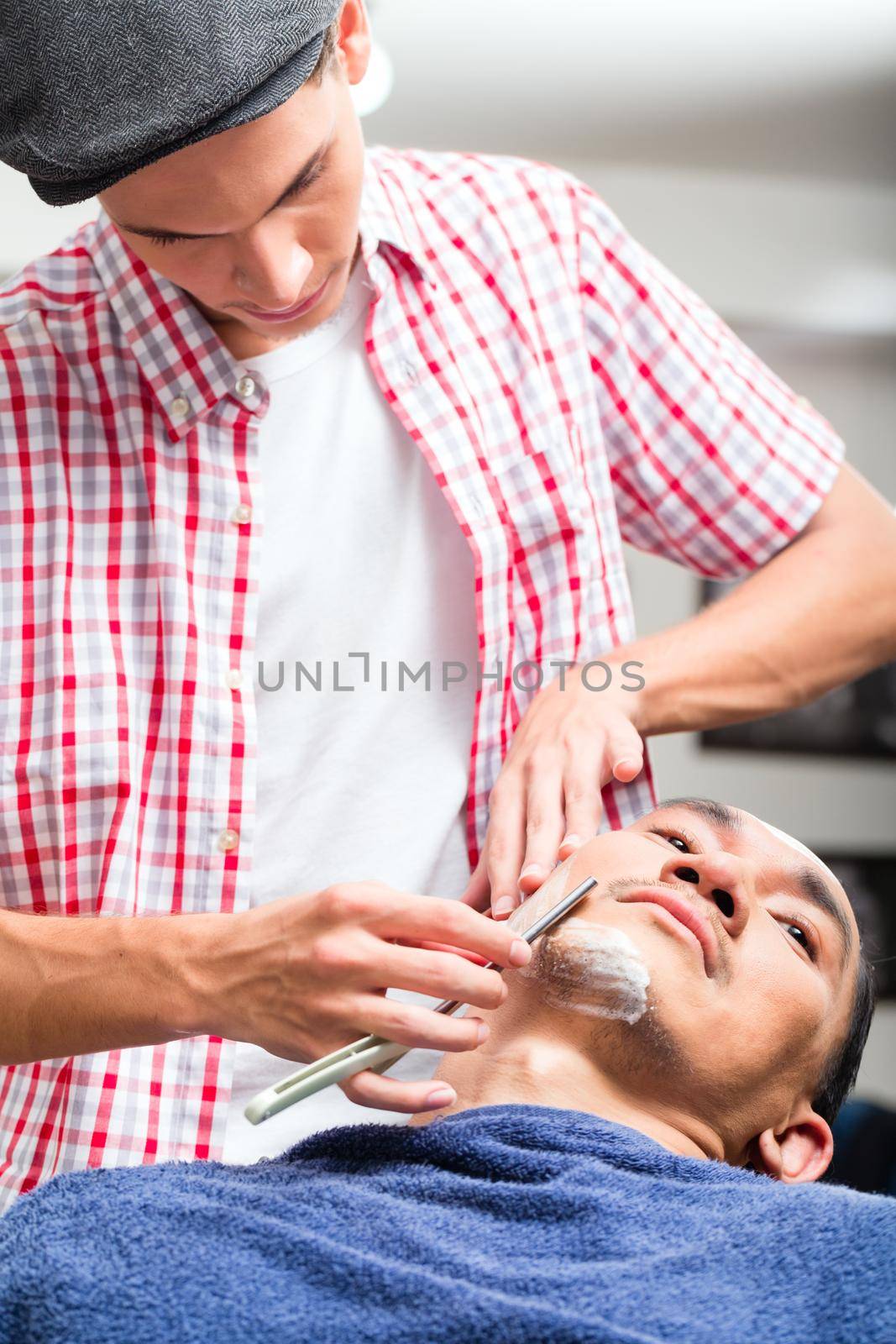 Close-up of hairdresser shaving with straight razor in salon