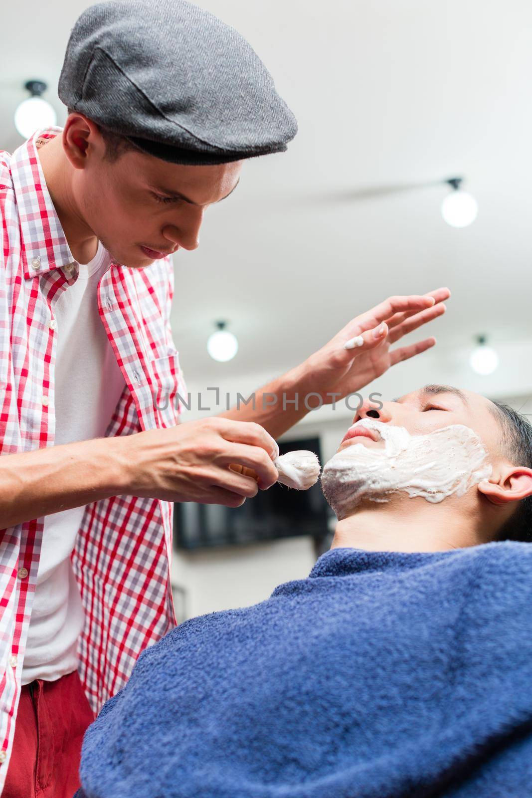 Barber putting some shaving cream on a client before shaving his beard in a barber shop