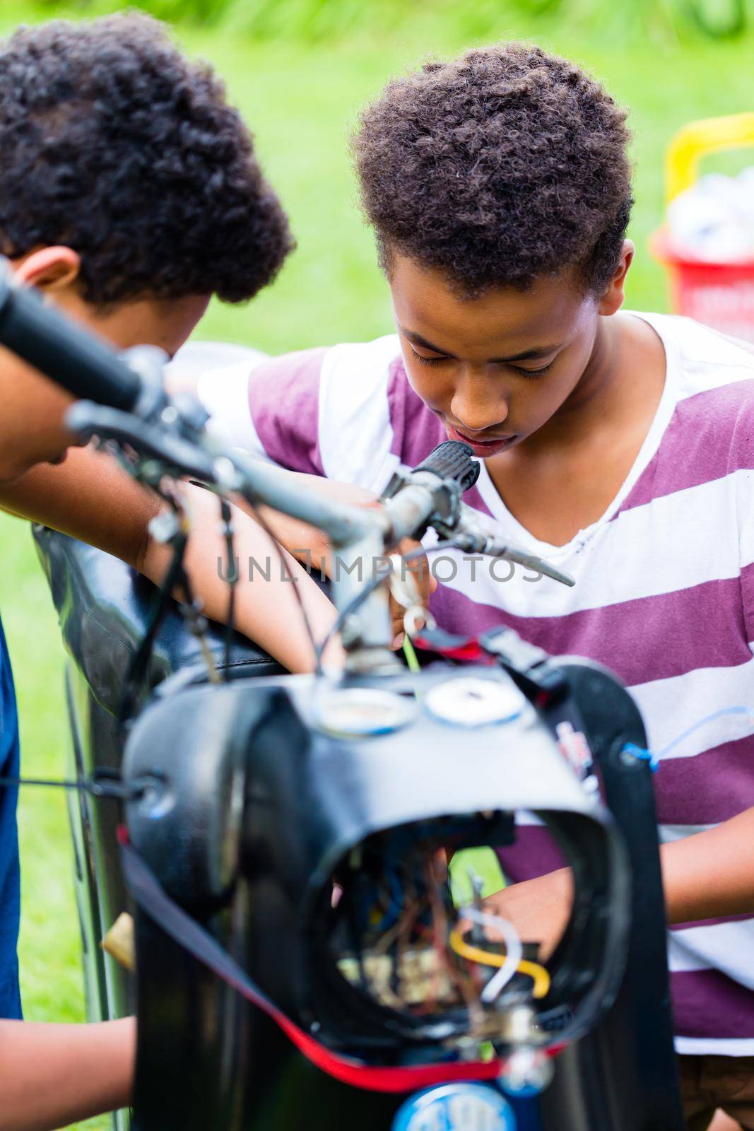 Close-up of two boys repairing an old fashioned motobike outdoors