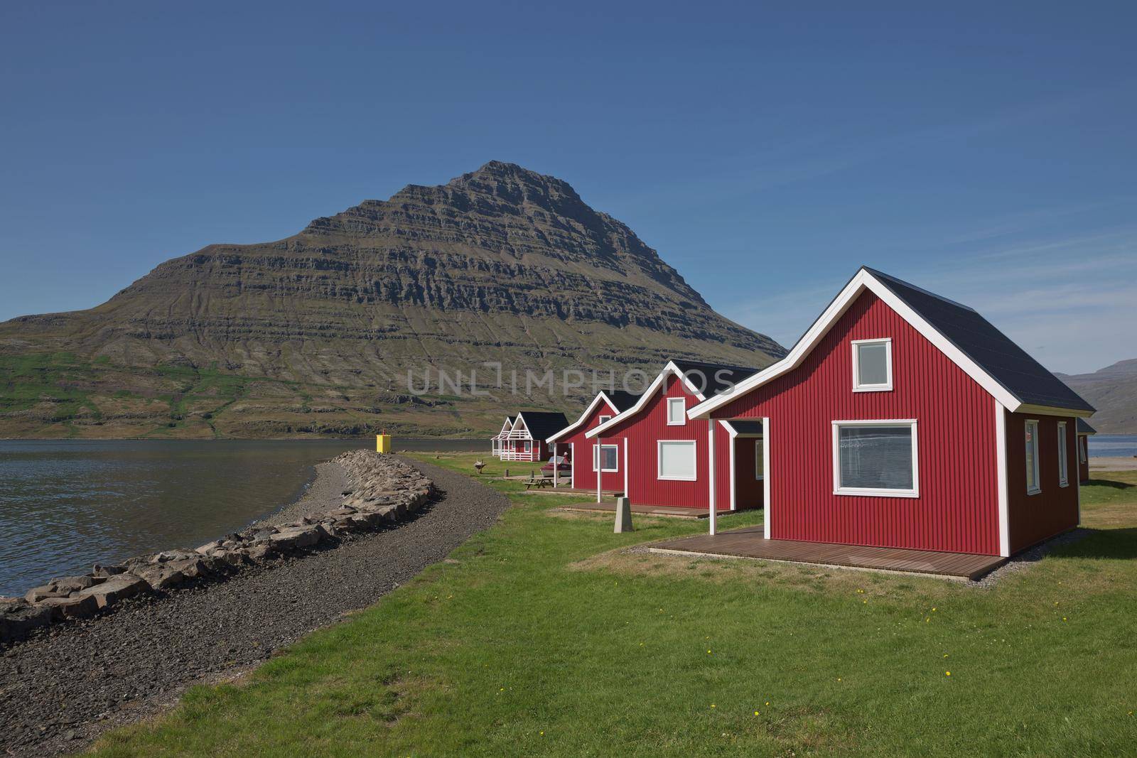 Traditional red painted wooden panel house with mighty Holmatindur mountain in the background in Eskifjordur, East Iceland.