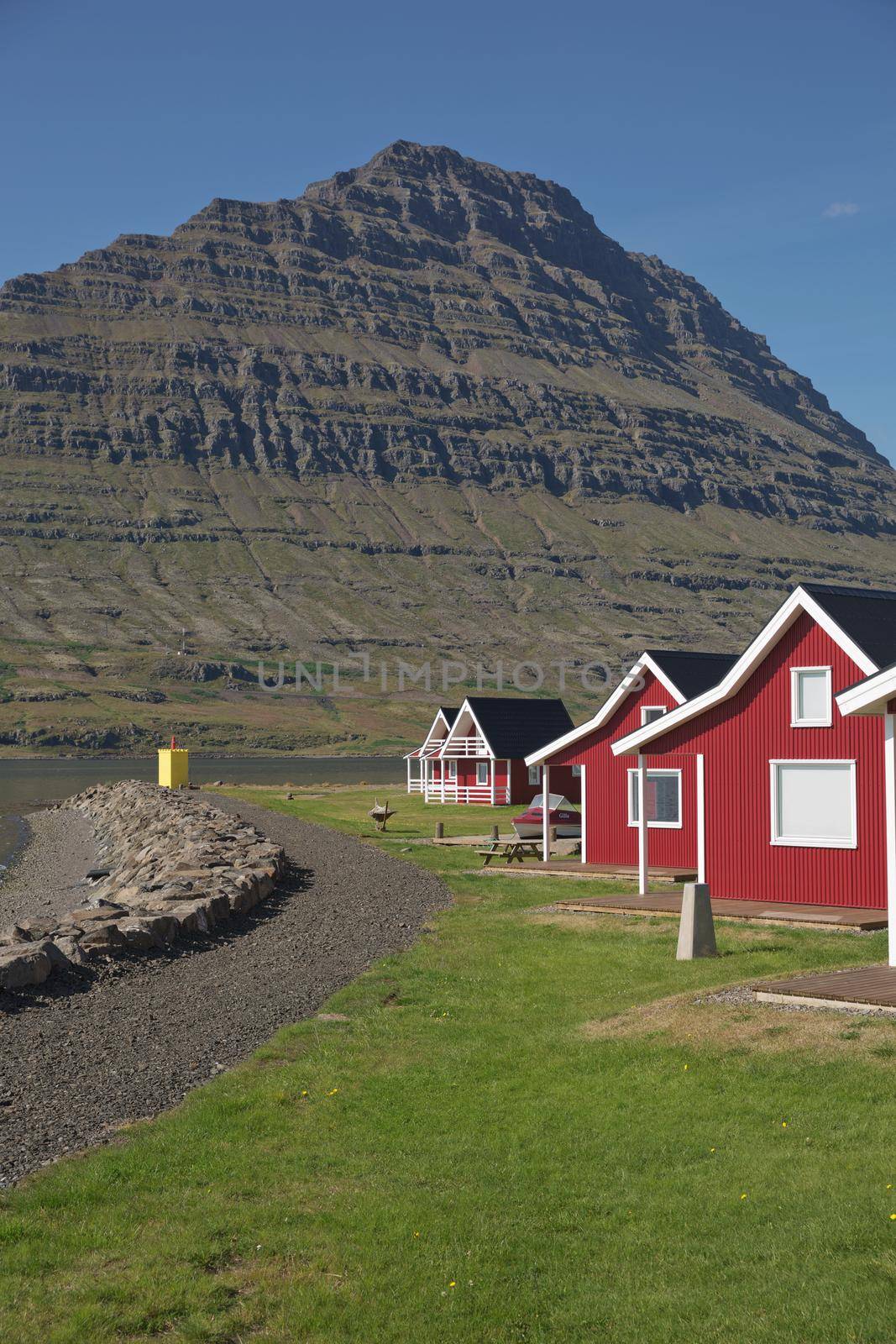 Traditional red painted wooden panel house with mighty Holmatindur mountain in the background in Eskifjordur, East Iceland.