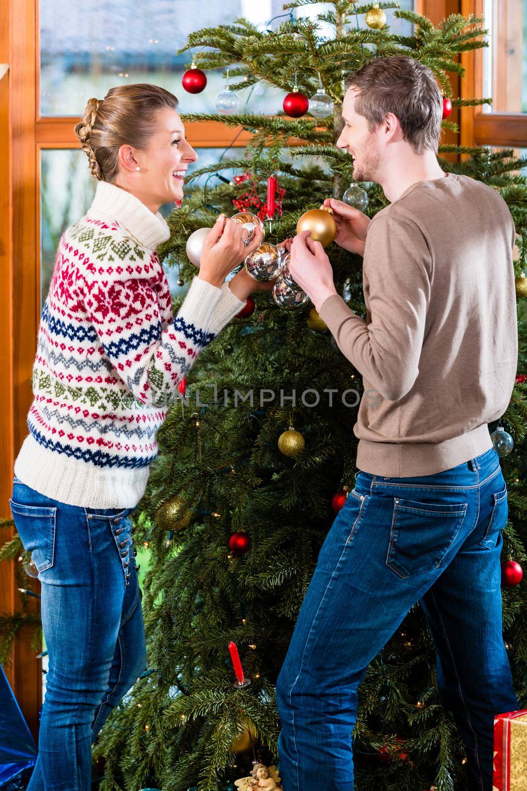 Young couple decorating fir tree for Christmas eve by Kzenon