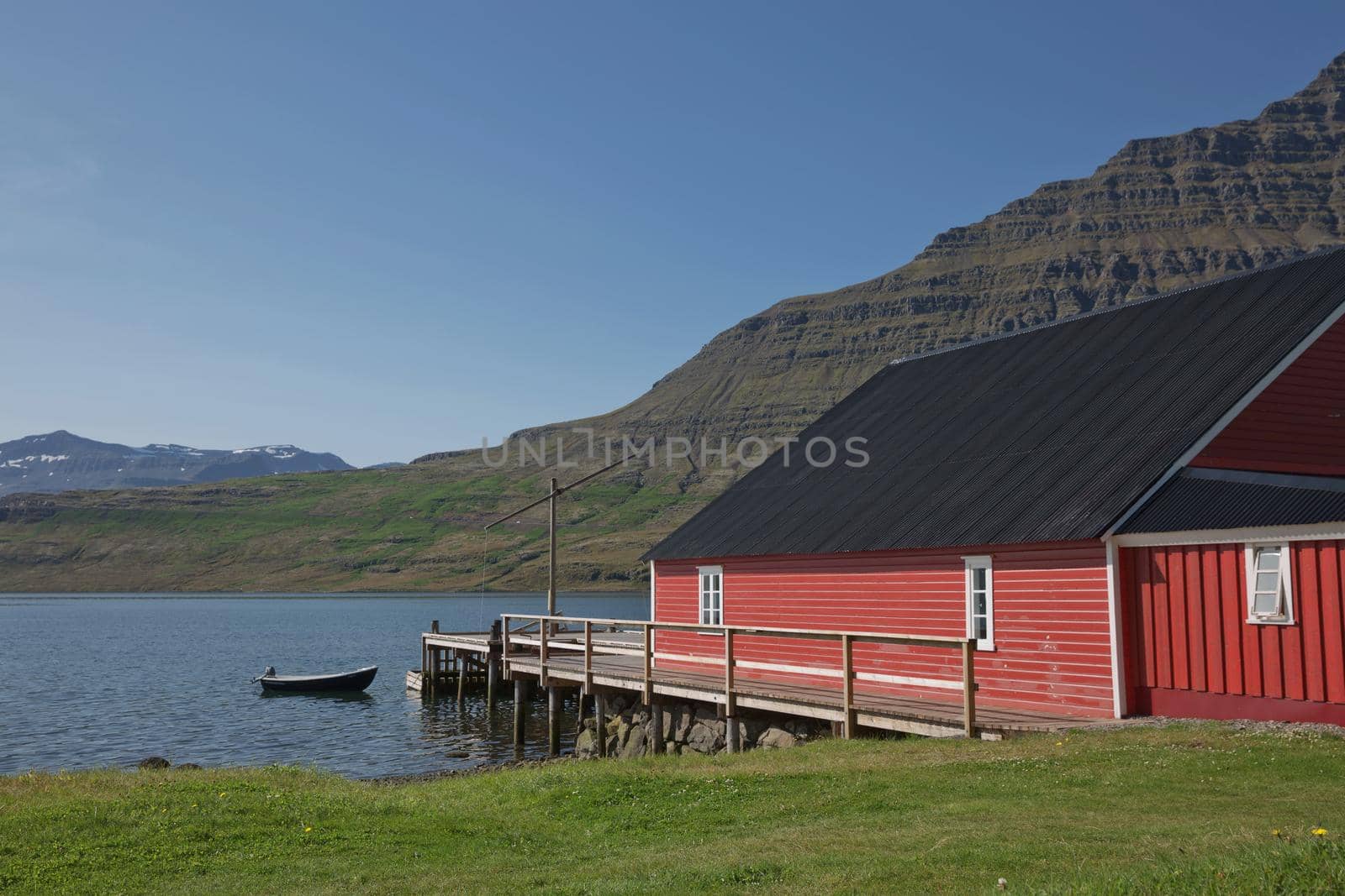 Traditional red painted wooden panel house with mighty Holmatindur mountain in the background in Eskifjordur, East Iceland.