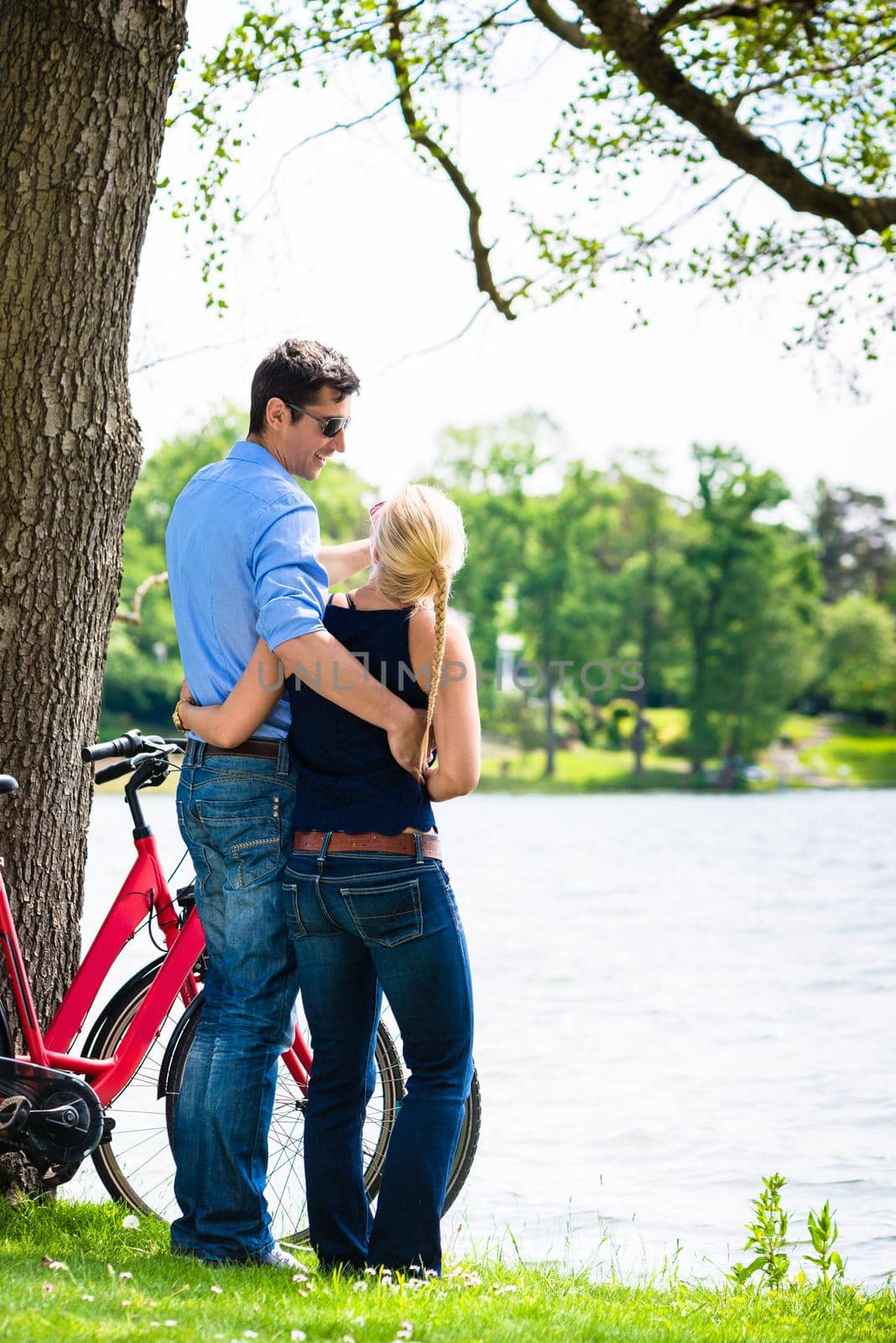 Rear view of young couple standing near the lake with bicycle