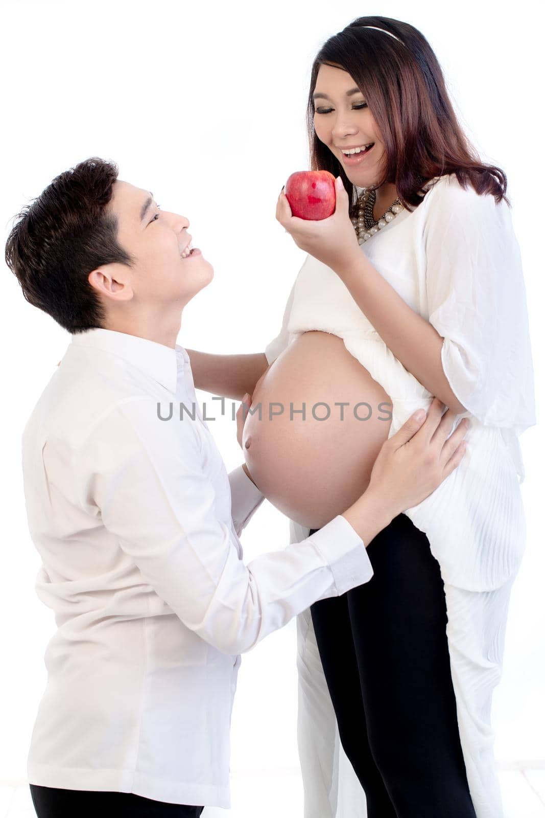 Happy pregnant wife holding an apple standing with his husband over white background