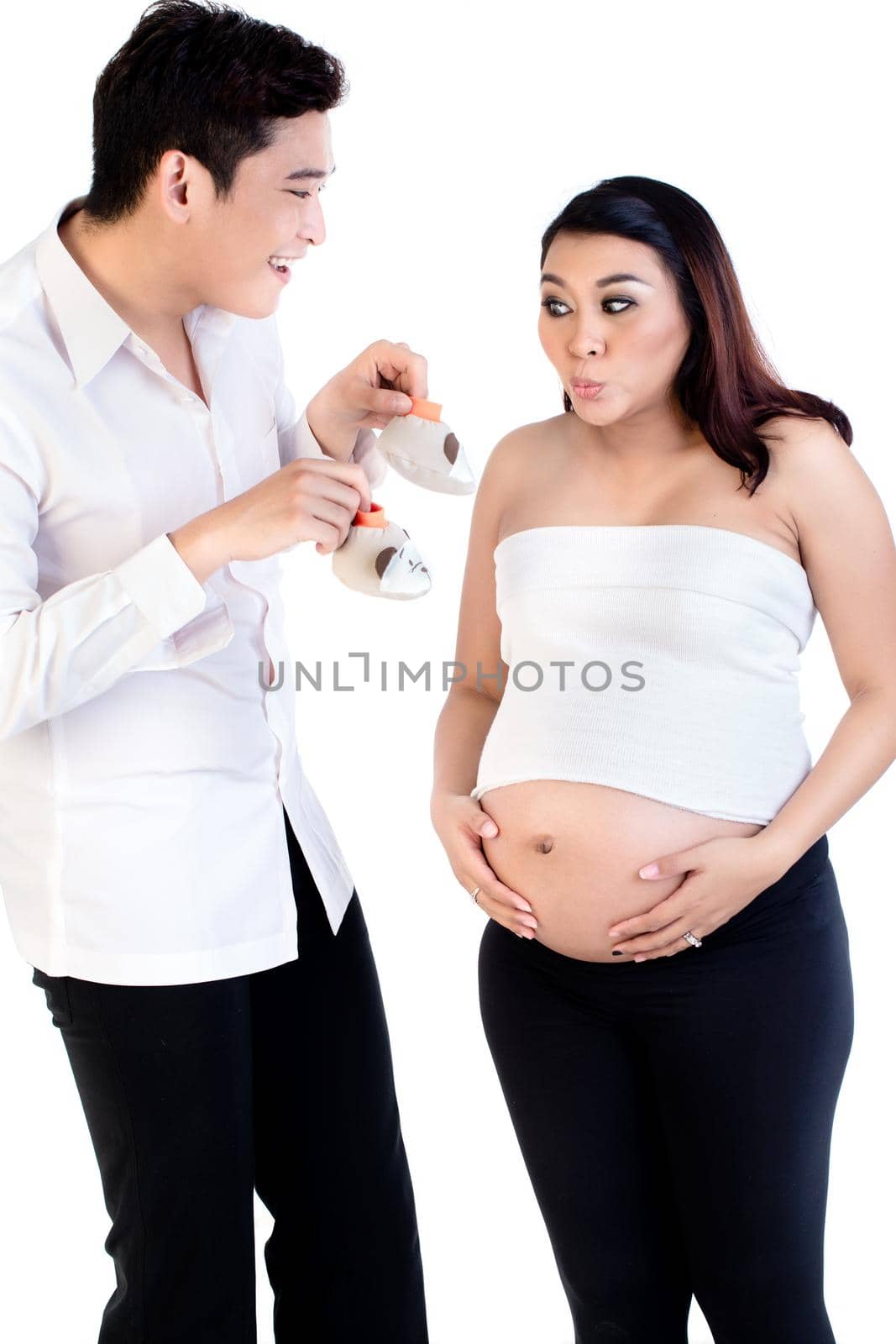 Smiling man showing her pregnant wife pair of baby shoes isolated on white background