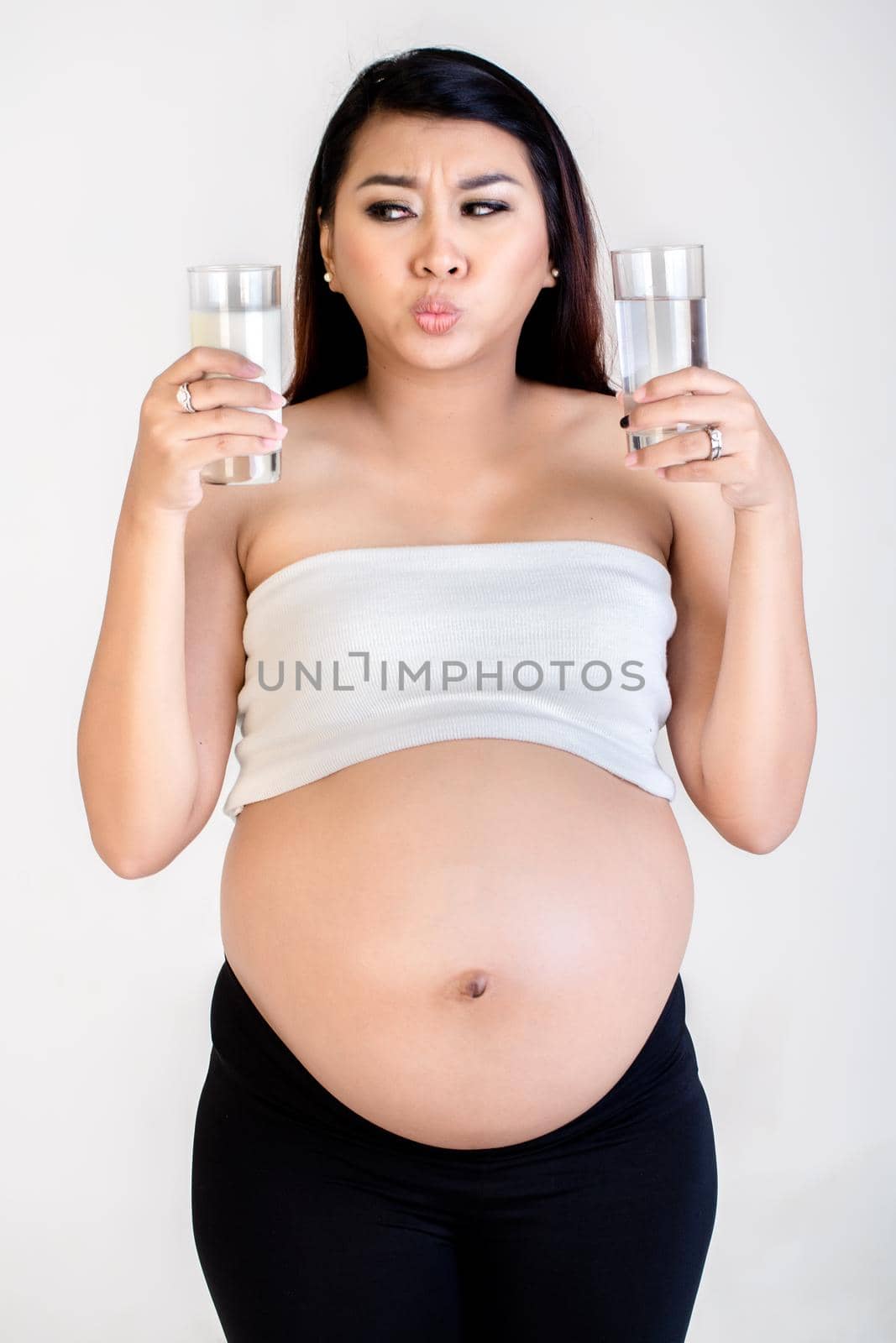 Close-up of confused pregnant woman holding milk and water glass isolated over white background