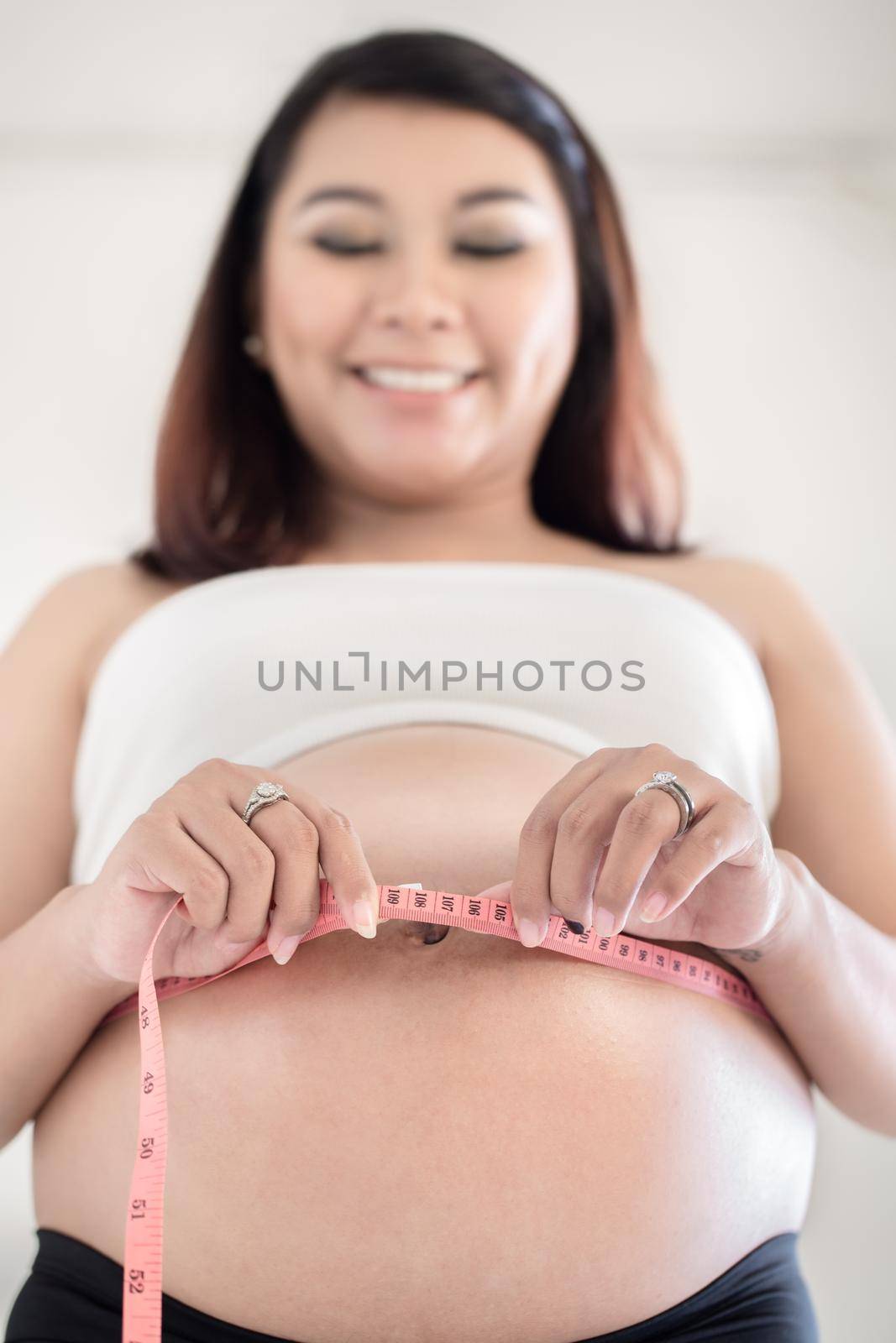 Close-up of smiling pregnant woman taking measurement of her belly