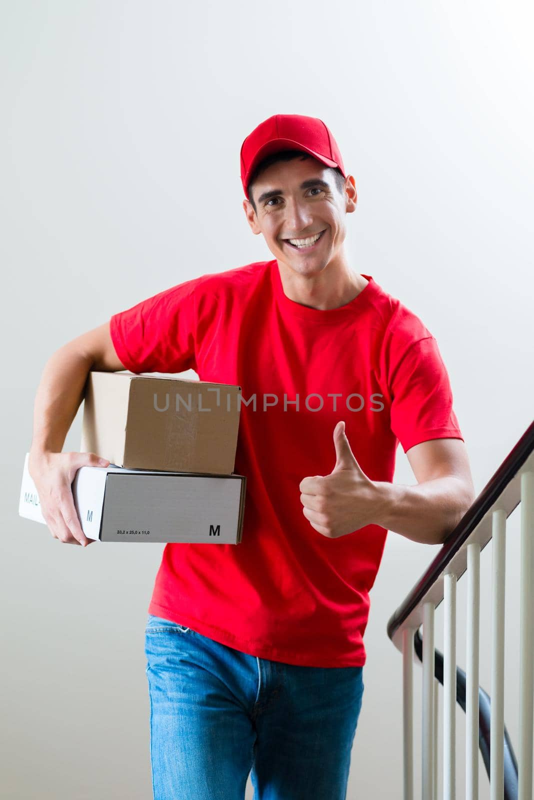 Delivery man holding mail boxes showing thumbsup by Kzenon