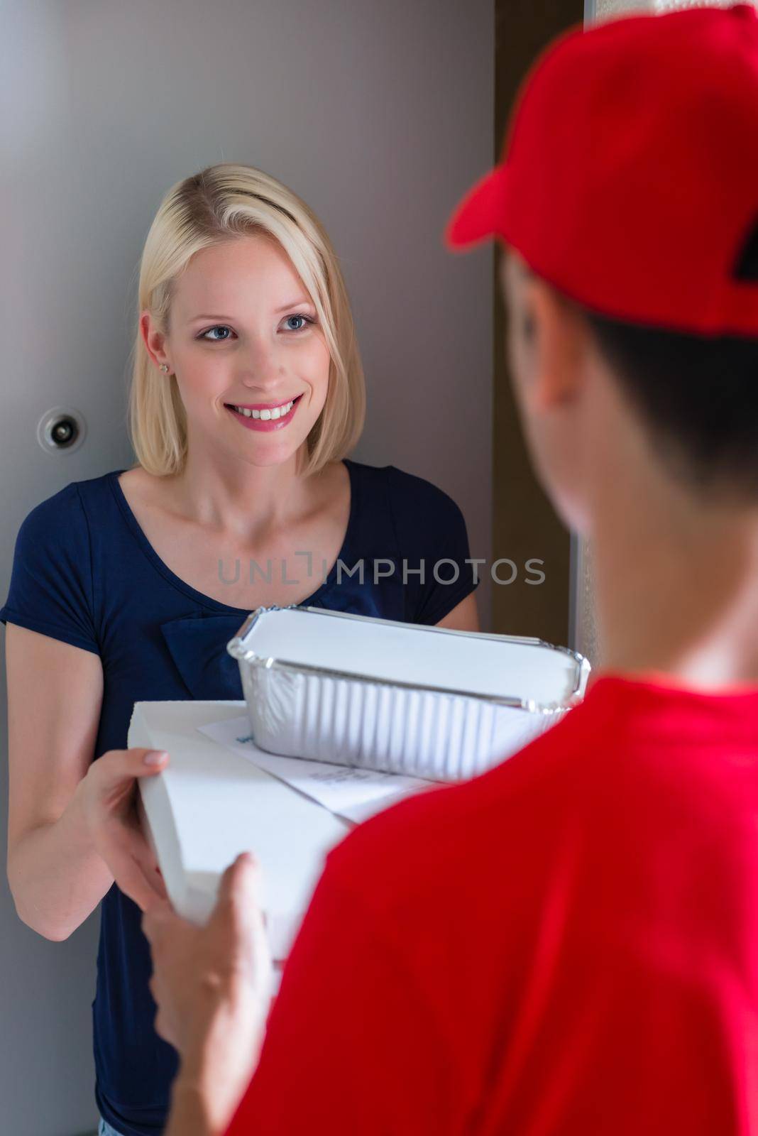 Happy young blonde woman taking fast food parcel at door from delivery man