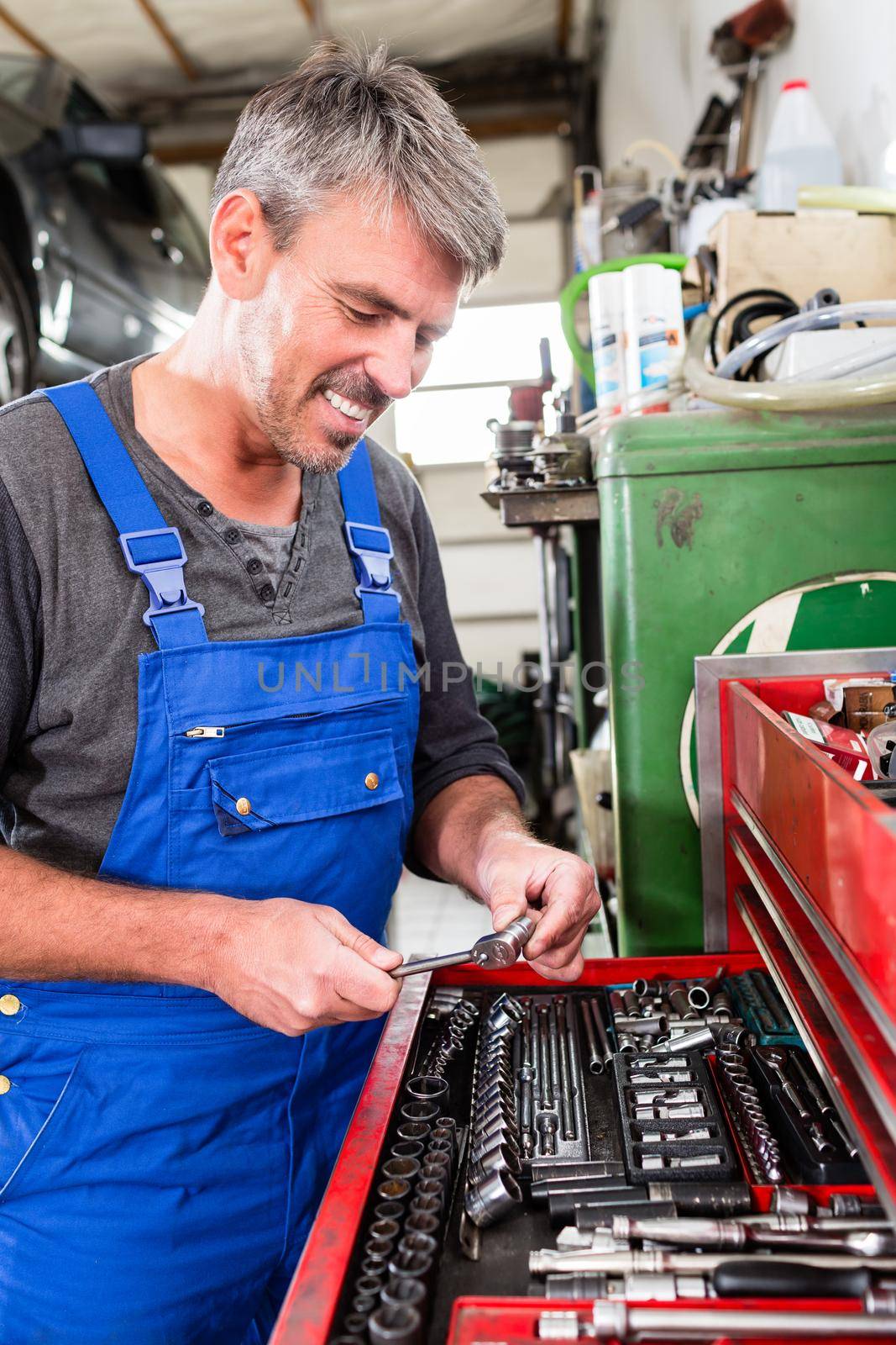 Smiling mature mechanic picked a tool from red tool box for car repair