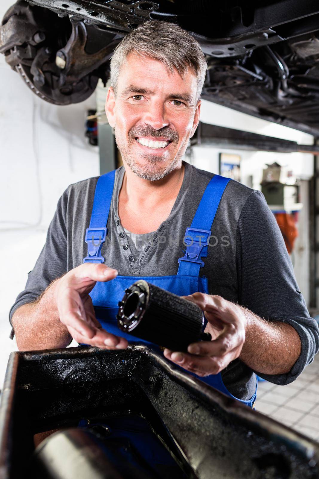 Smiling mature man holding the oil filter of a car by Kzenon